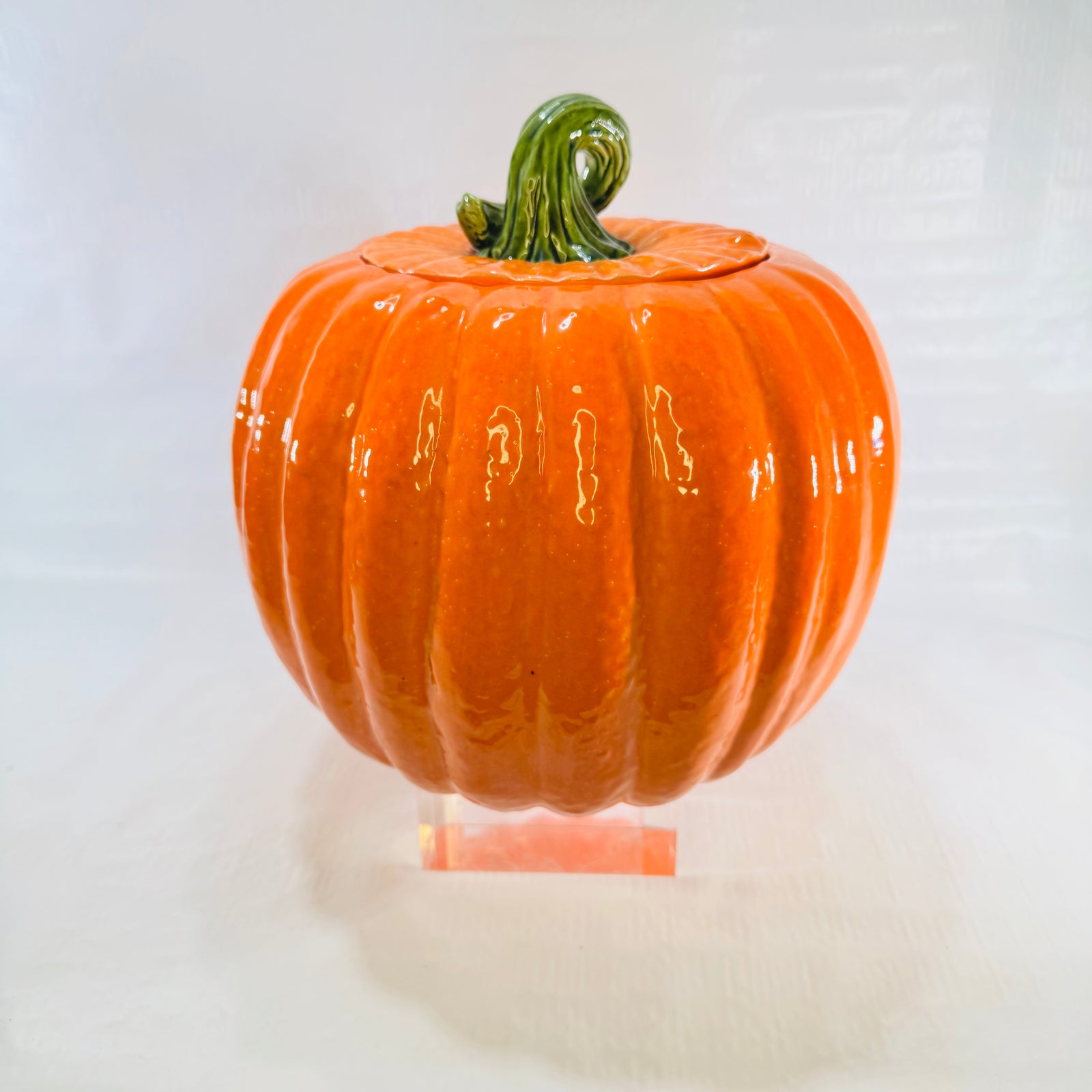 Front view of a glossy orange ceramic pumpkin cookie jar with green stem lid