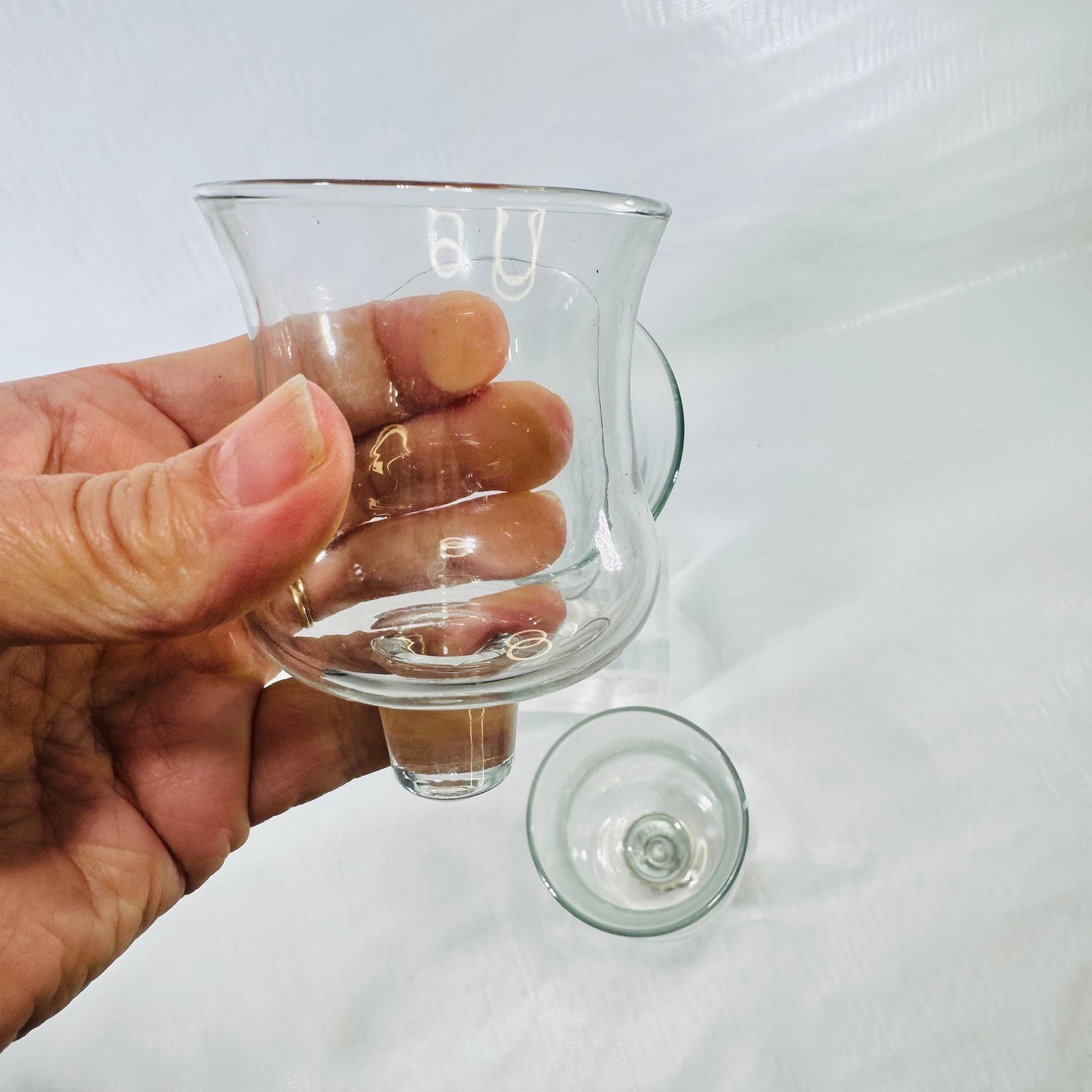 Small clear glass peg votive cup held in hand, showing its bare glass peg.