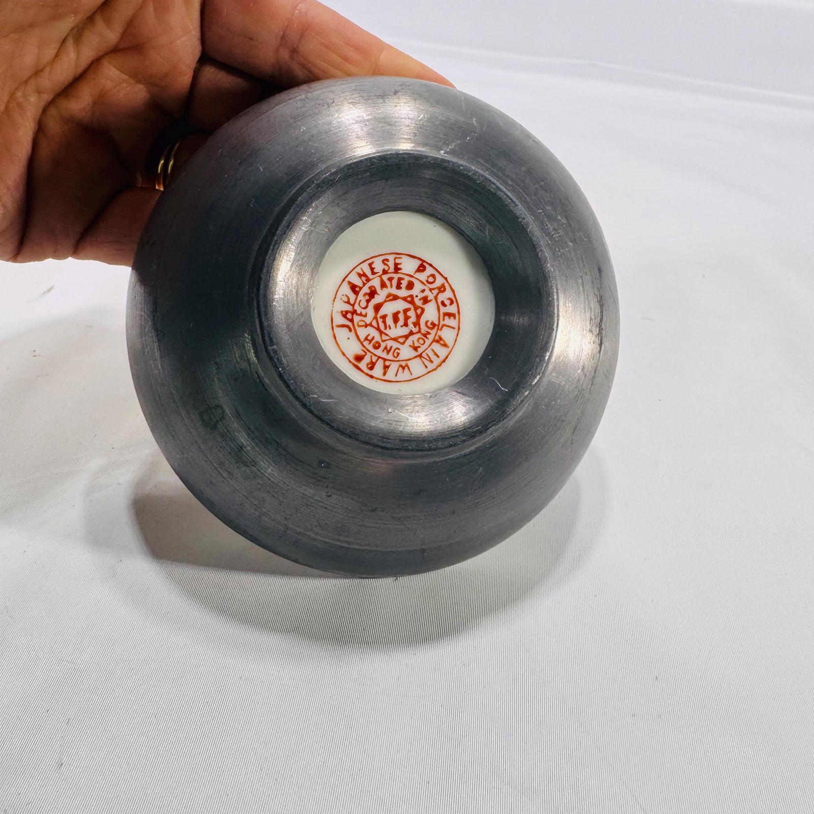 Underside of cloisonné bowl with a white circular porcelain insert stamped “Chinese Porcelain Inlaid in Hong Kong,” set into a dark metal base.