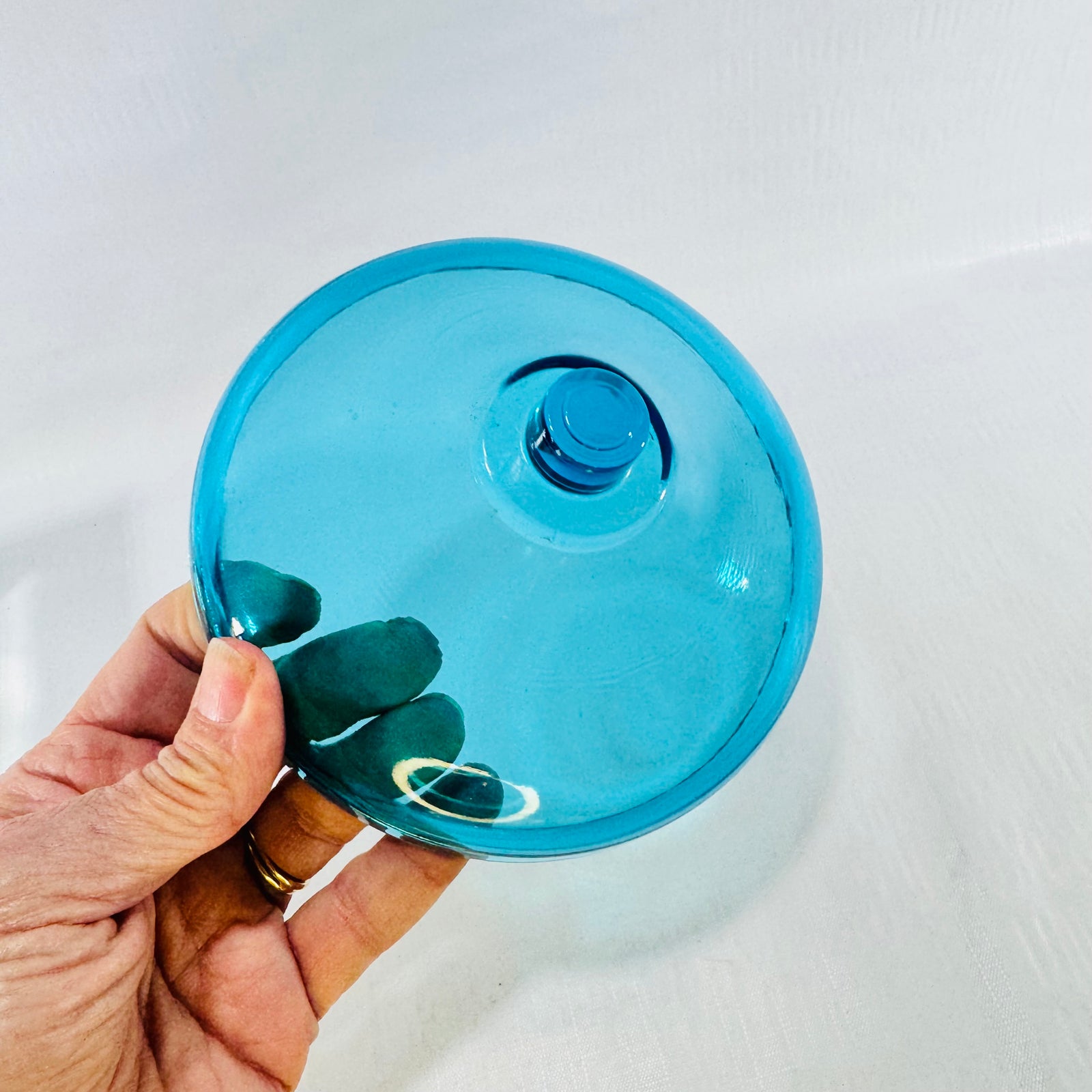 Turquoise blue glass fairy lamp bobeche held in a hand, showing the round tier and center knob