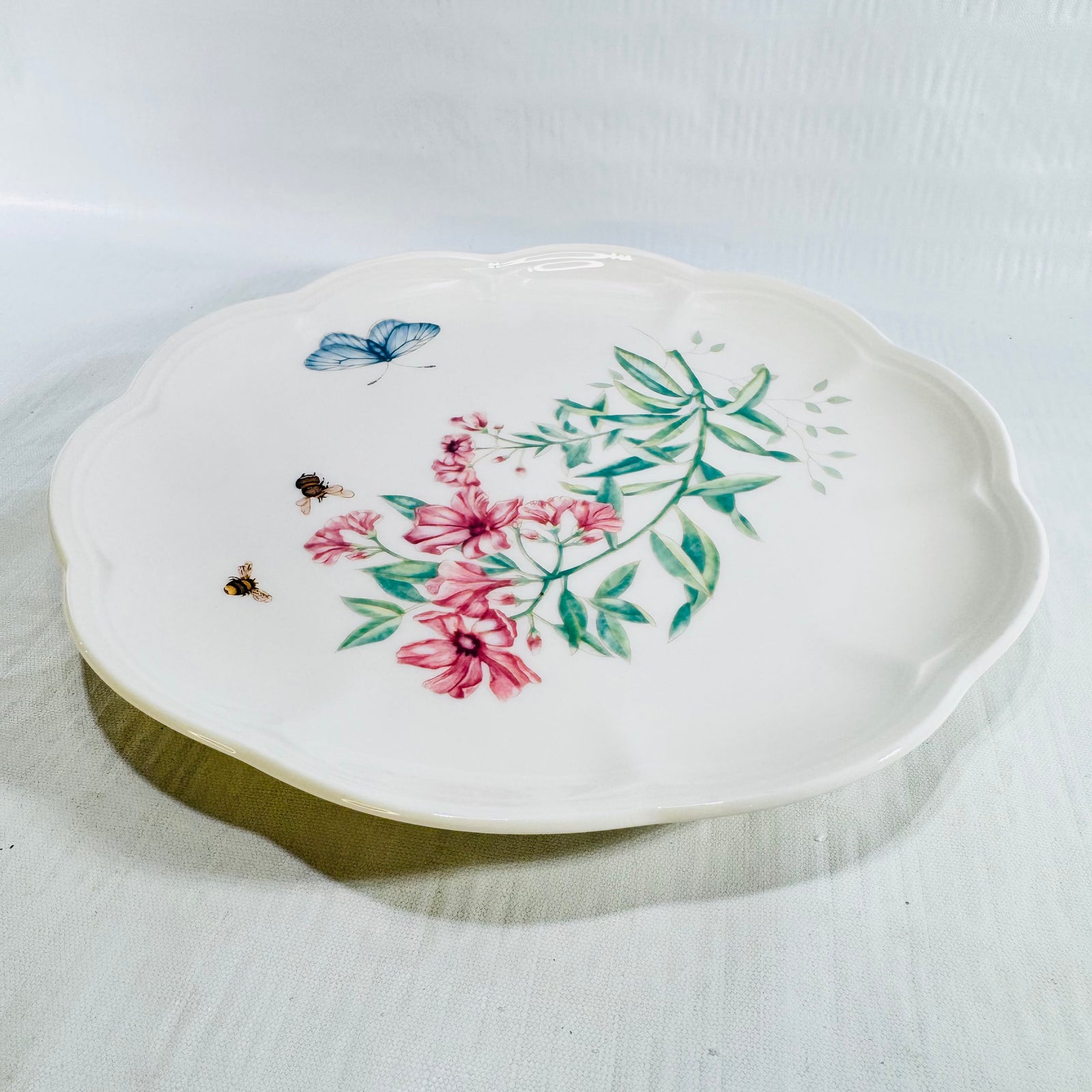 Angled view of Lenox Butterfly Meadow Swallowtail 9 inch plate on white fabric with pink wisteria