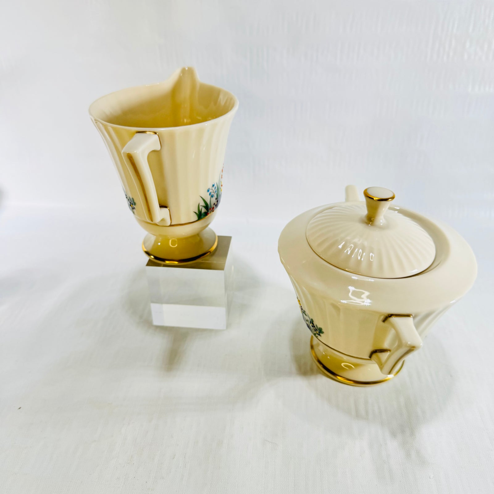 Lenox Rutledge creamer on a clear stand beside the covered sugar bowl in a wide view
