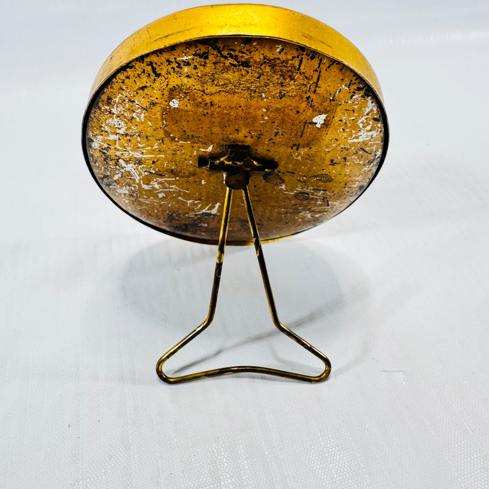 Back of the oval frame standing on its wire easel, with heavy scratching and worn metal.