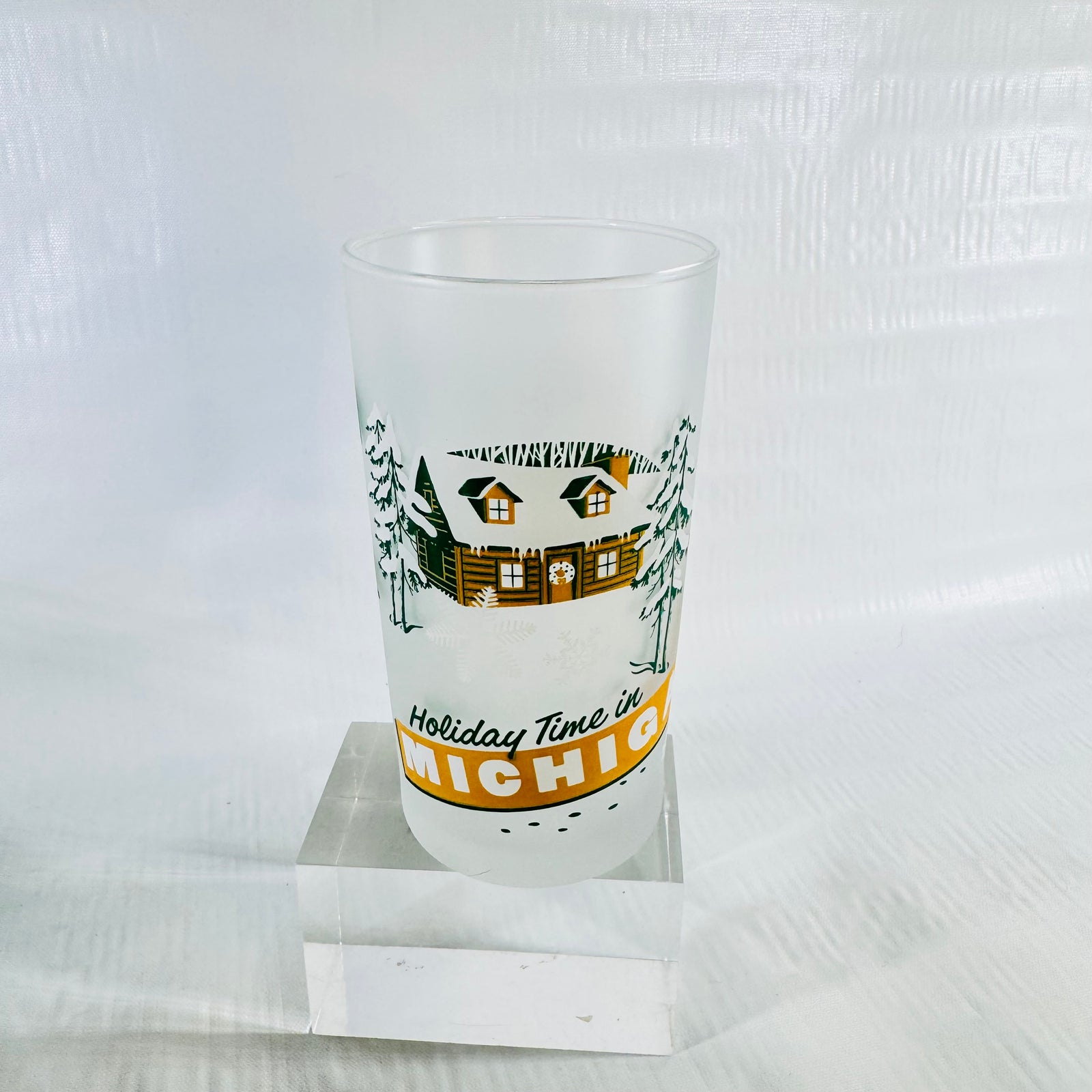 Frosted glass tumbler with a snowy log cabin, pine trees, and the Holiday Time in Michigan banner on the front.