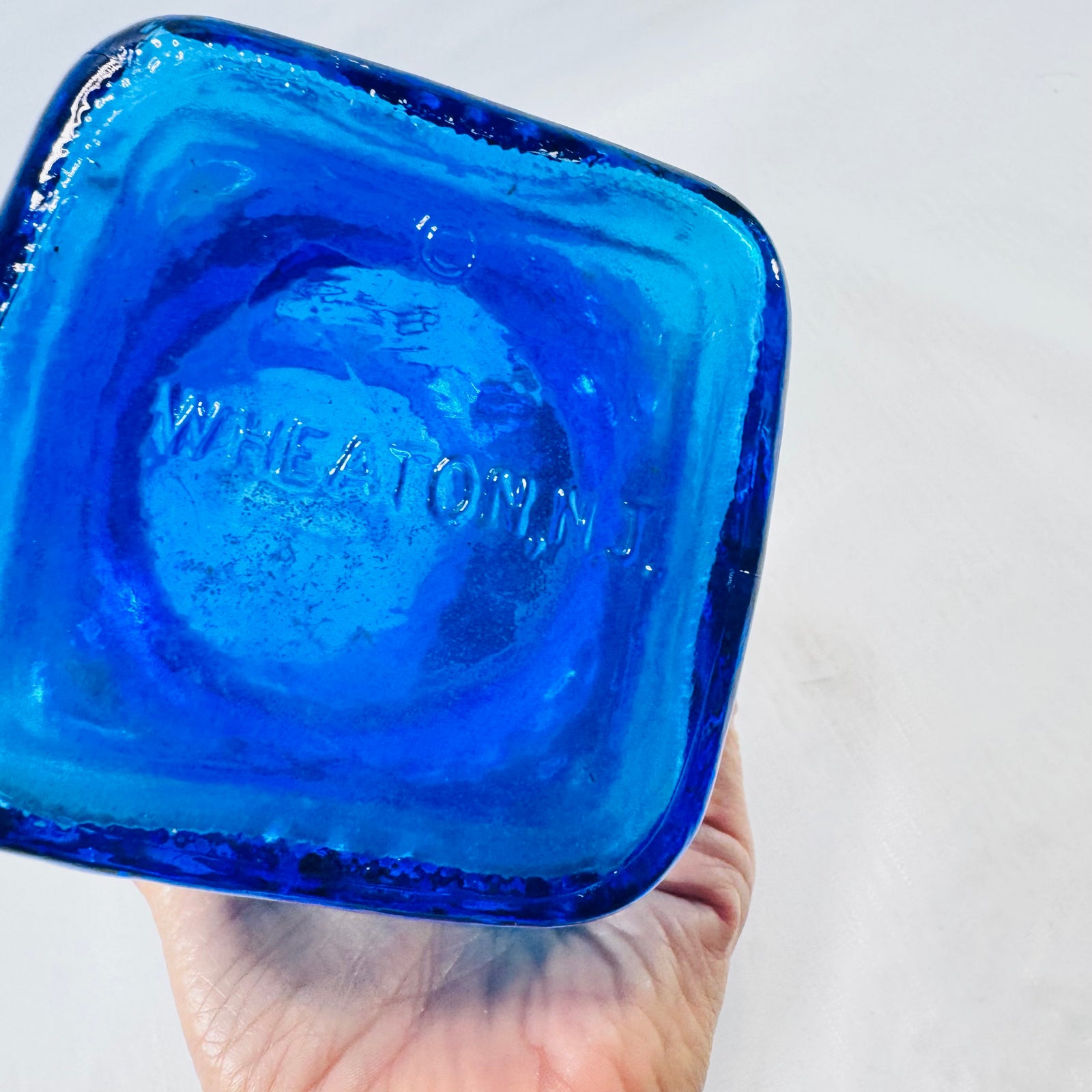 Bottom of the blue glass bank embossed WHEATON N.J. with a small round emblem.