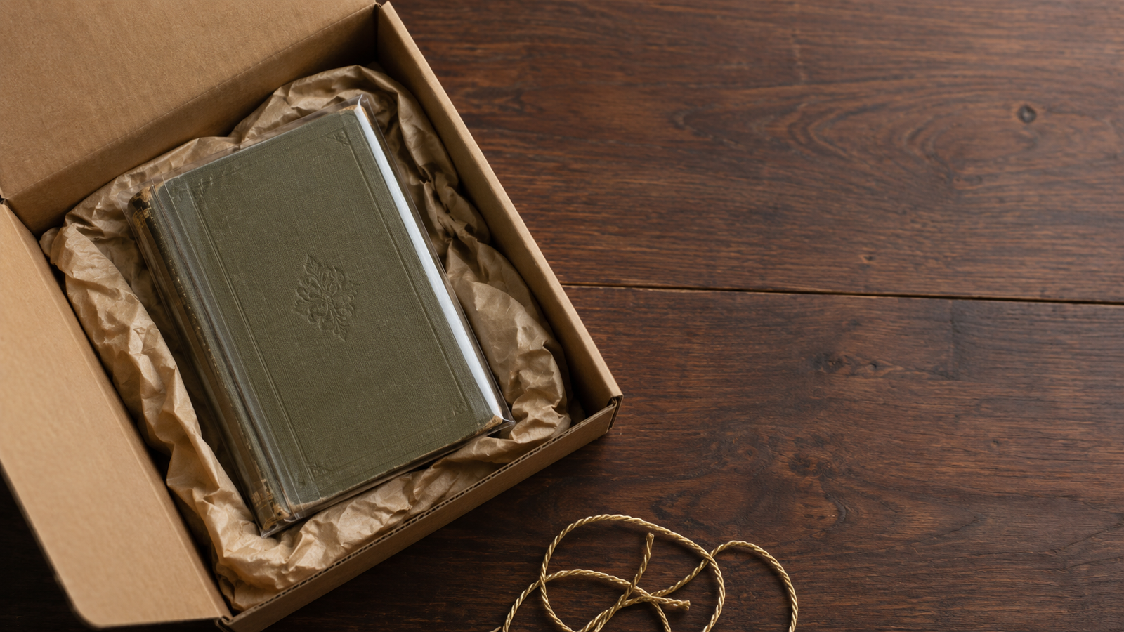 A vintage book wrapped in protective padding beside an open cushioned cardboard shipping box on a bright ivory surface.