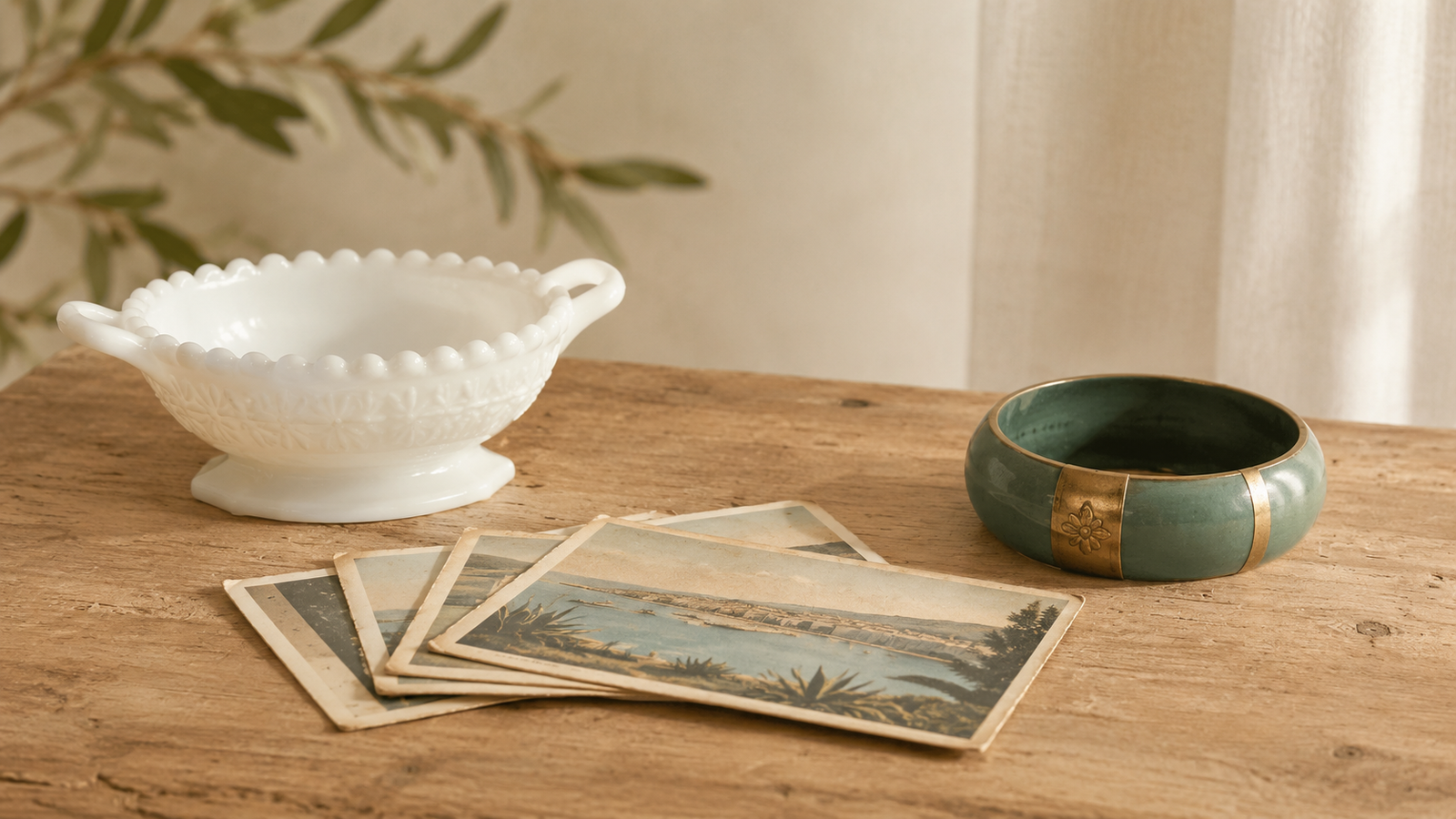 A quiet still life of overlooked vintage pieces, including a plain milk glass dish, old postcards, and a bangle.