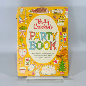 1960 Betty Crocker’s Party Book—bright yellow illustrated ring-bound vintage cookbook with colorful “PARTY BOOK” lettering and festive icons.