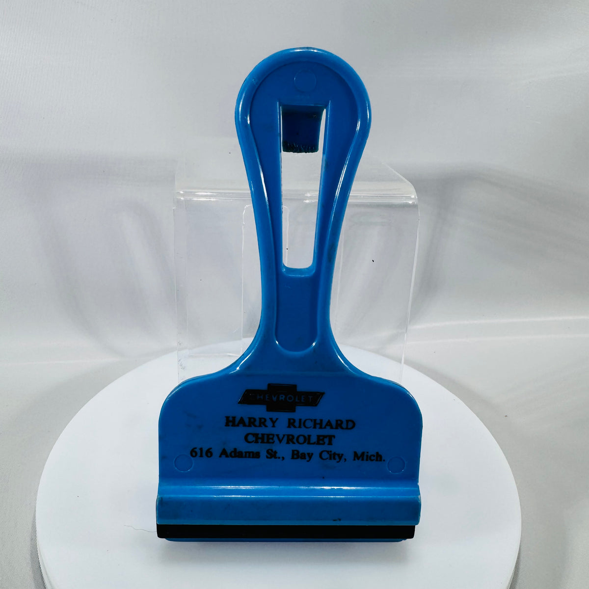 Blue vintage Chevrolet dealer ice scraper with black rubber blade and “Harry Richard Chevrolet, 616 Adams St., Bay City, Mich.” printed on front.