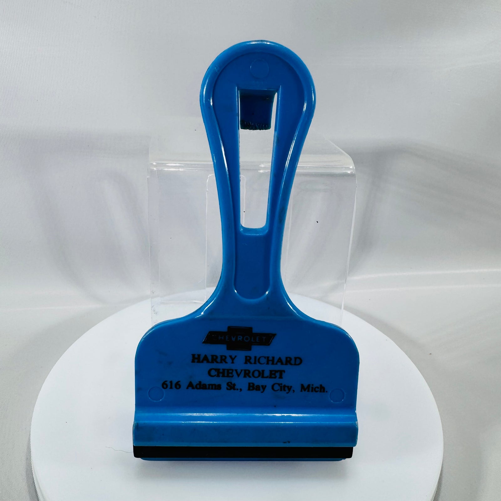 Blue vintage Chevrolet dealer ice scraper with black rubber blade and “Harry Richard Chevrolet, 616 Adams St., Bay City, Mich.” printed on front.