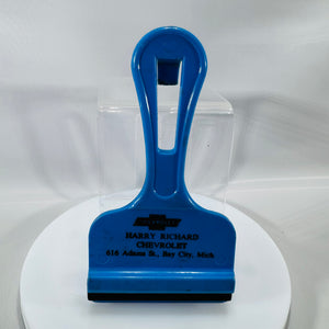 Blue vintage Chevrolet dealer ice scraper with black rubber blade and “Harry Richard Chevrolet, 616 Adams St., Bay City, Mich.” printed on front.