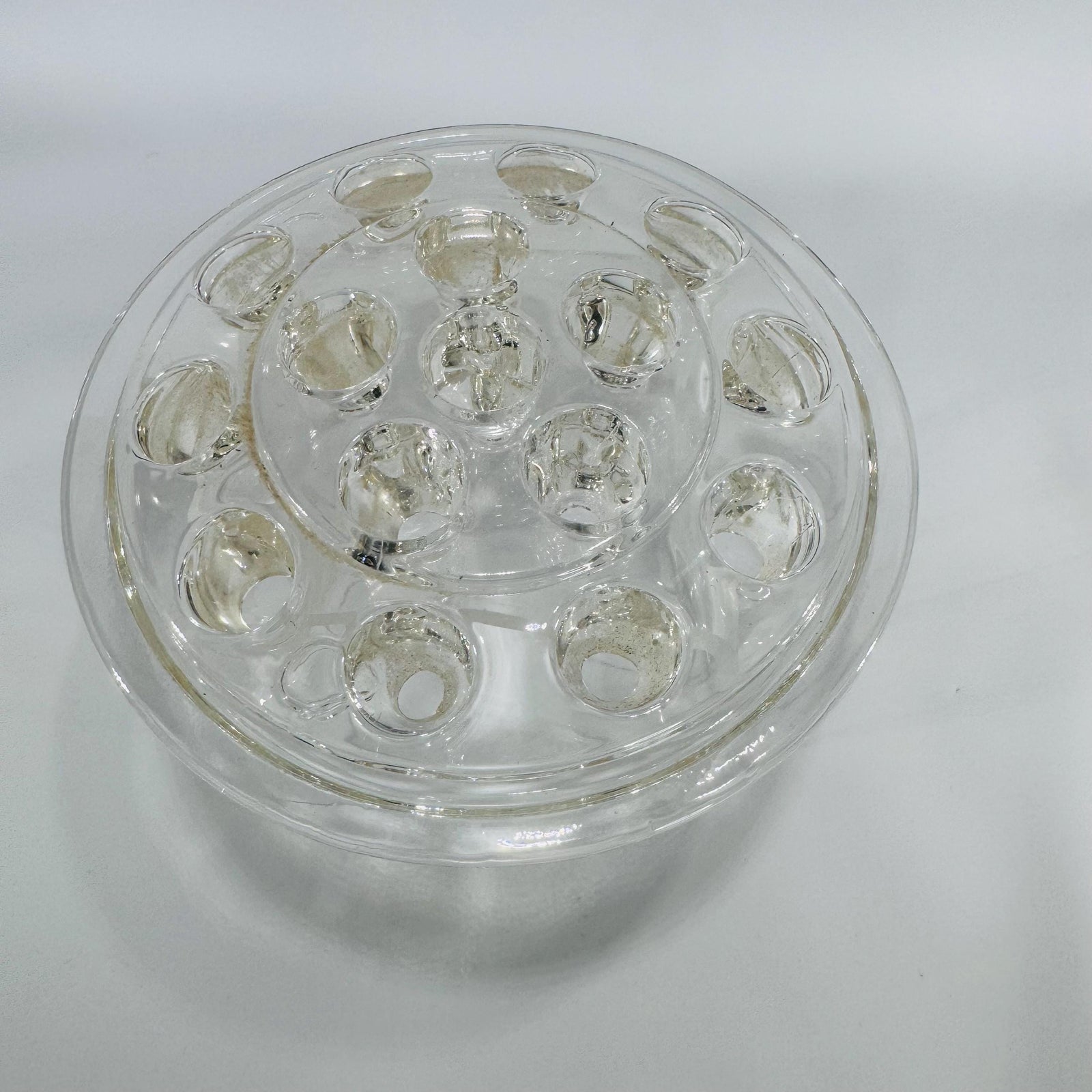 Clear round glass flower frog with multiple stem holes in a dome design, viewed from above