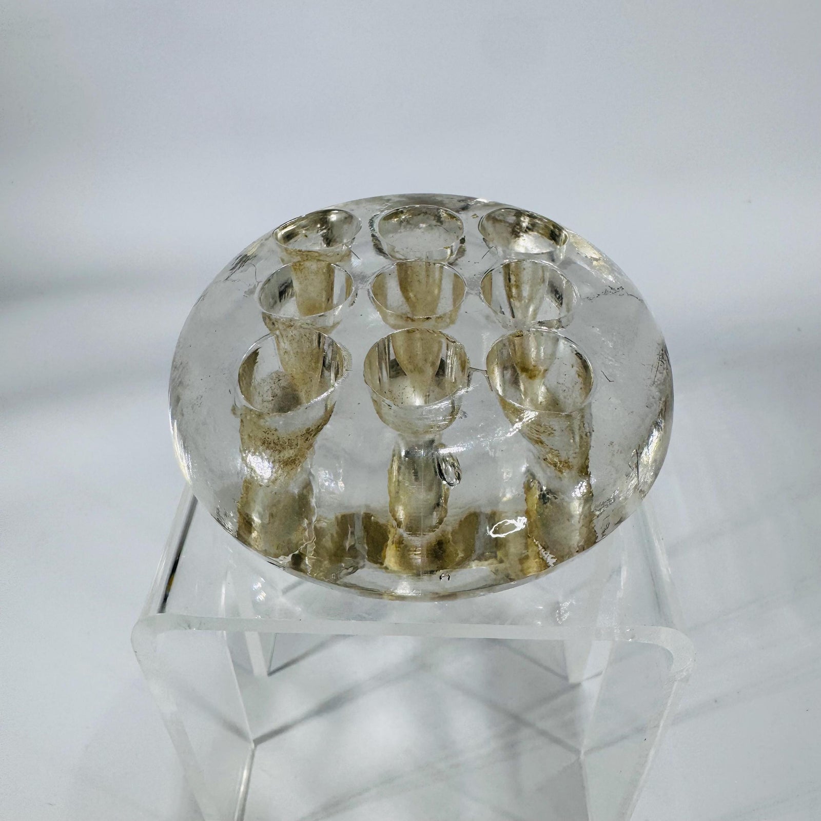 Clear round glass flower frog with 9 holes and footed base, 3 inches wide, shown on a stand.