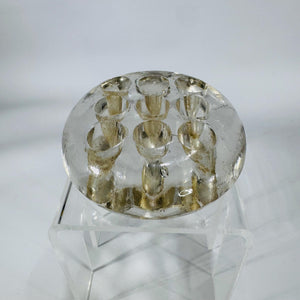 Clear round glass flower frog with 9 holes and footed base, 3 inches wide, shown on a stand.