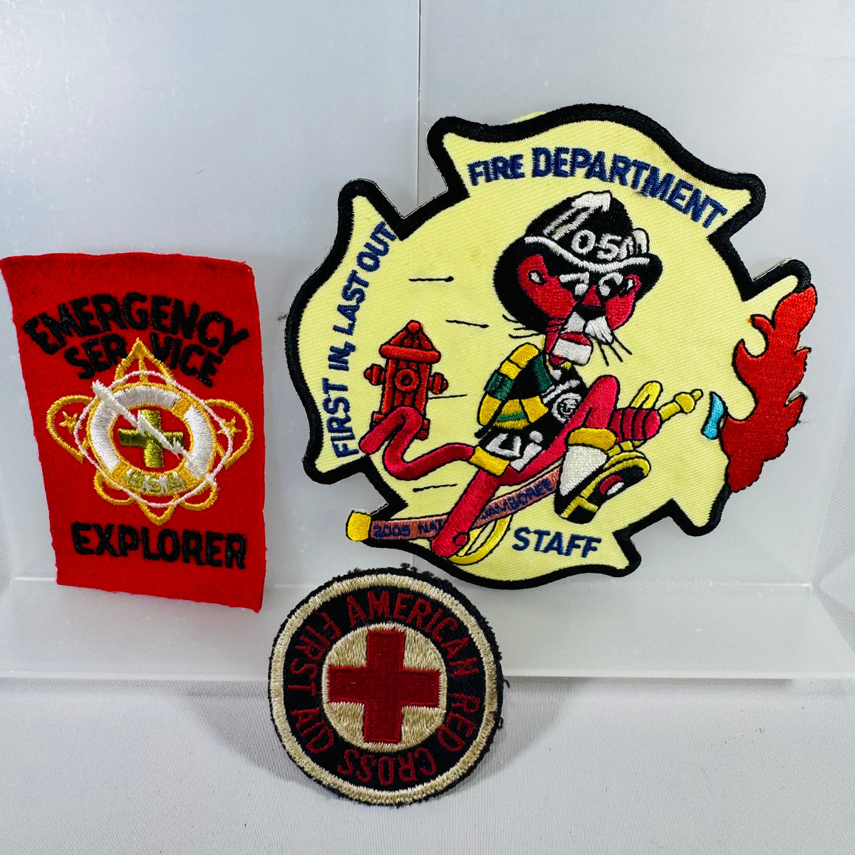 Three patches: a red 'Explorer' patch, a yellow 'Fire Department Staff' patch with a cartoon character, and a round 'American Red Cross' patch.
