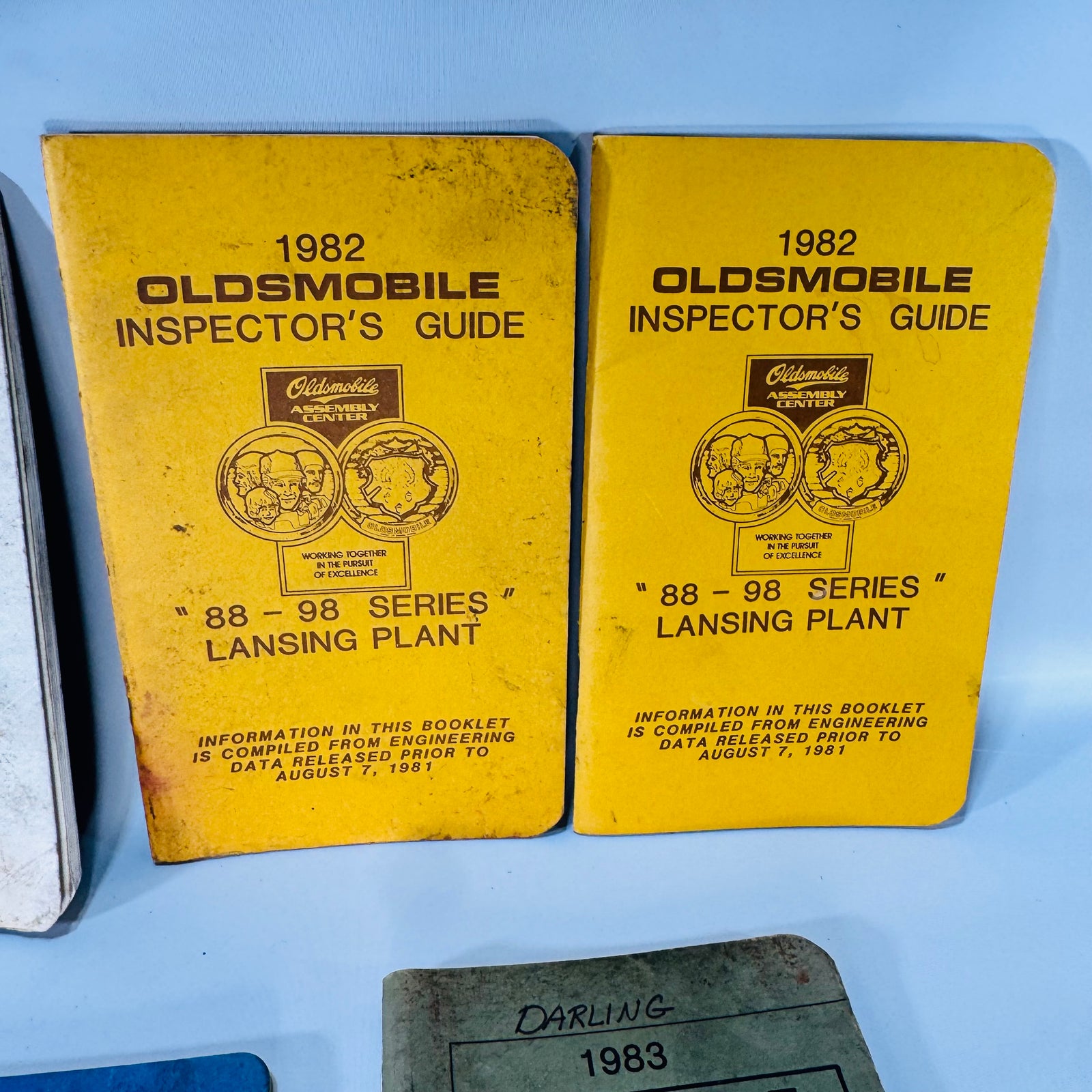 Seven vintage Oldsmobile Inspector’s Guide booklets (1981–1983) in mixed cover colors, stacked and laid out—shop-worn Lansing Plant 88–98 and Cutlass series references.