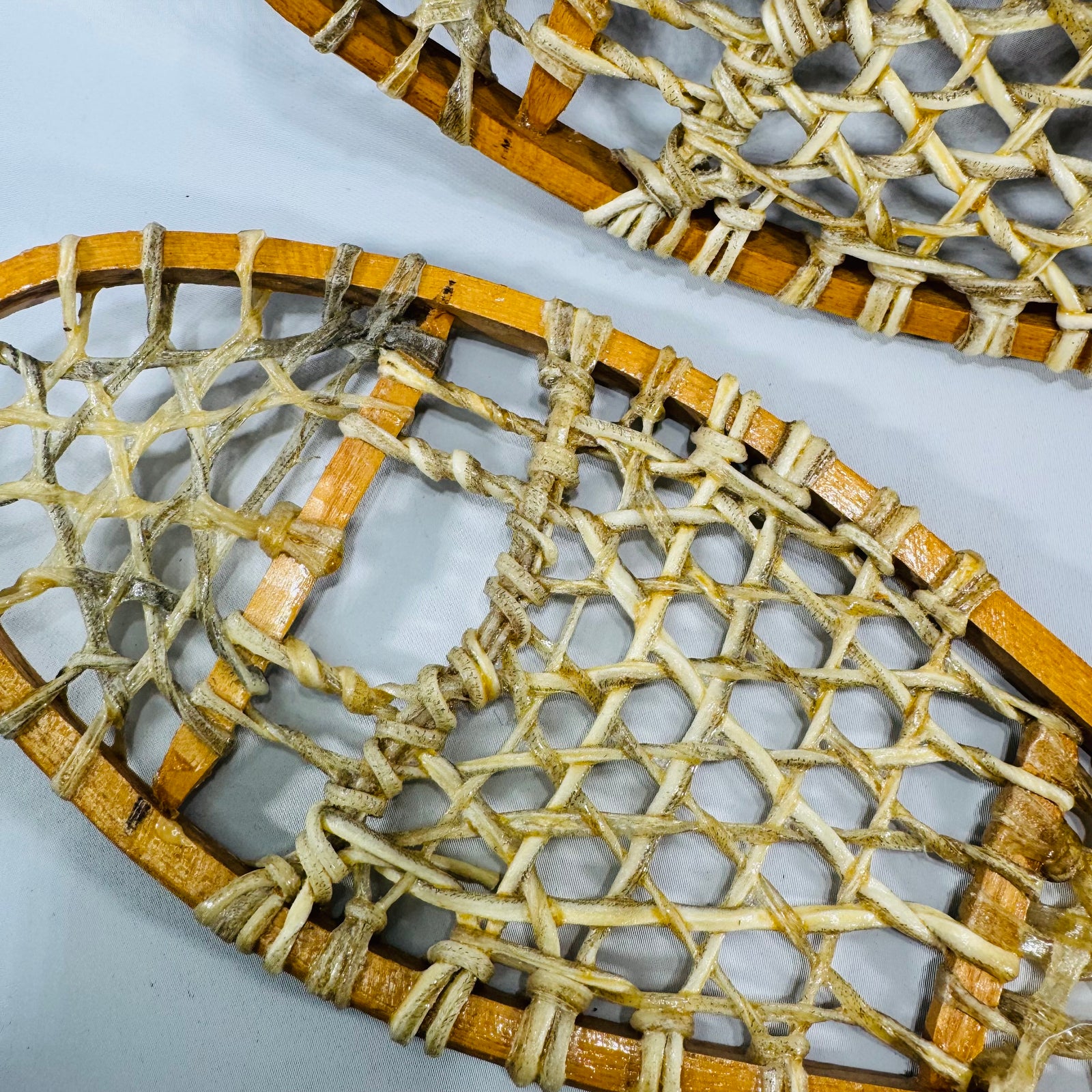 Pair of vintage salesman sample miniature wooden snowshoes with cream rawhide lacing on a white background, 16-inch cabin lodge wall decor.