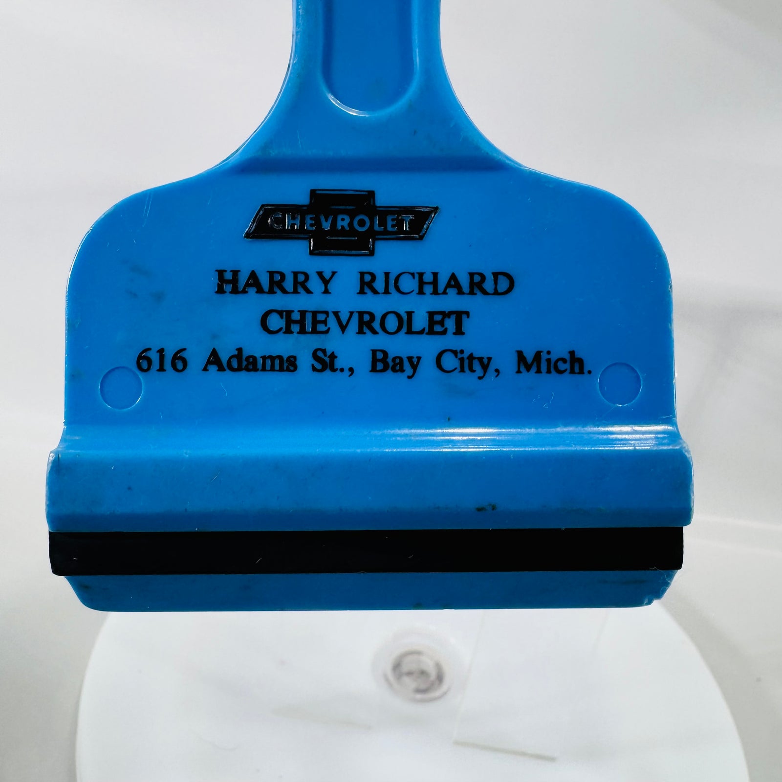 Blue vintage Chevrolet dealer ice scraper with black rubber blade and “Harry Richard Chevrolet, 616 Adams St., Bay City, Mich.” printed on front.