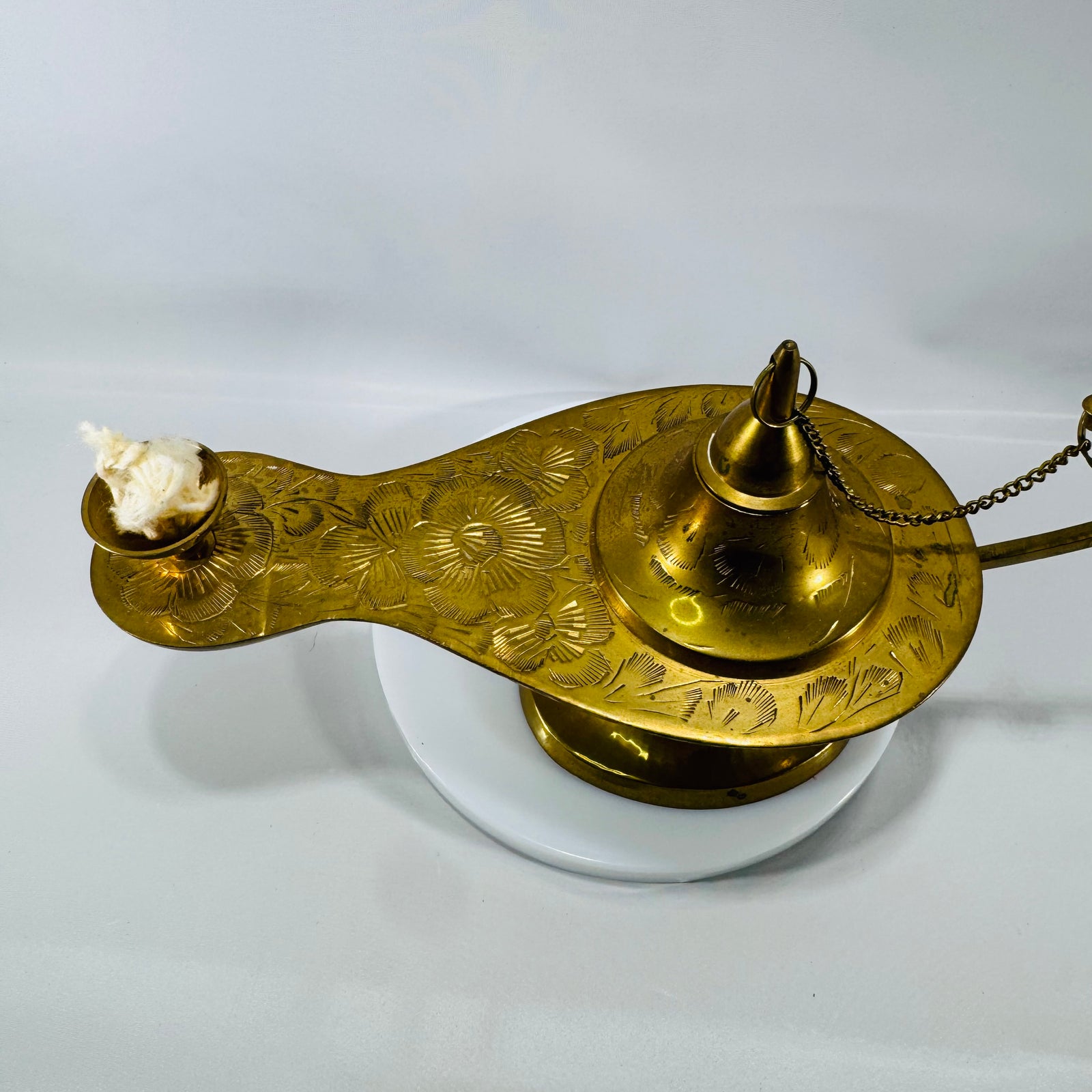 Vintage etched brass Aladdin-style genie lamp with chain-attached lid and wick cup, photographed on a white background.