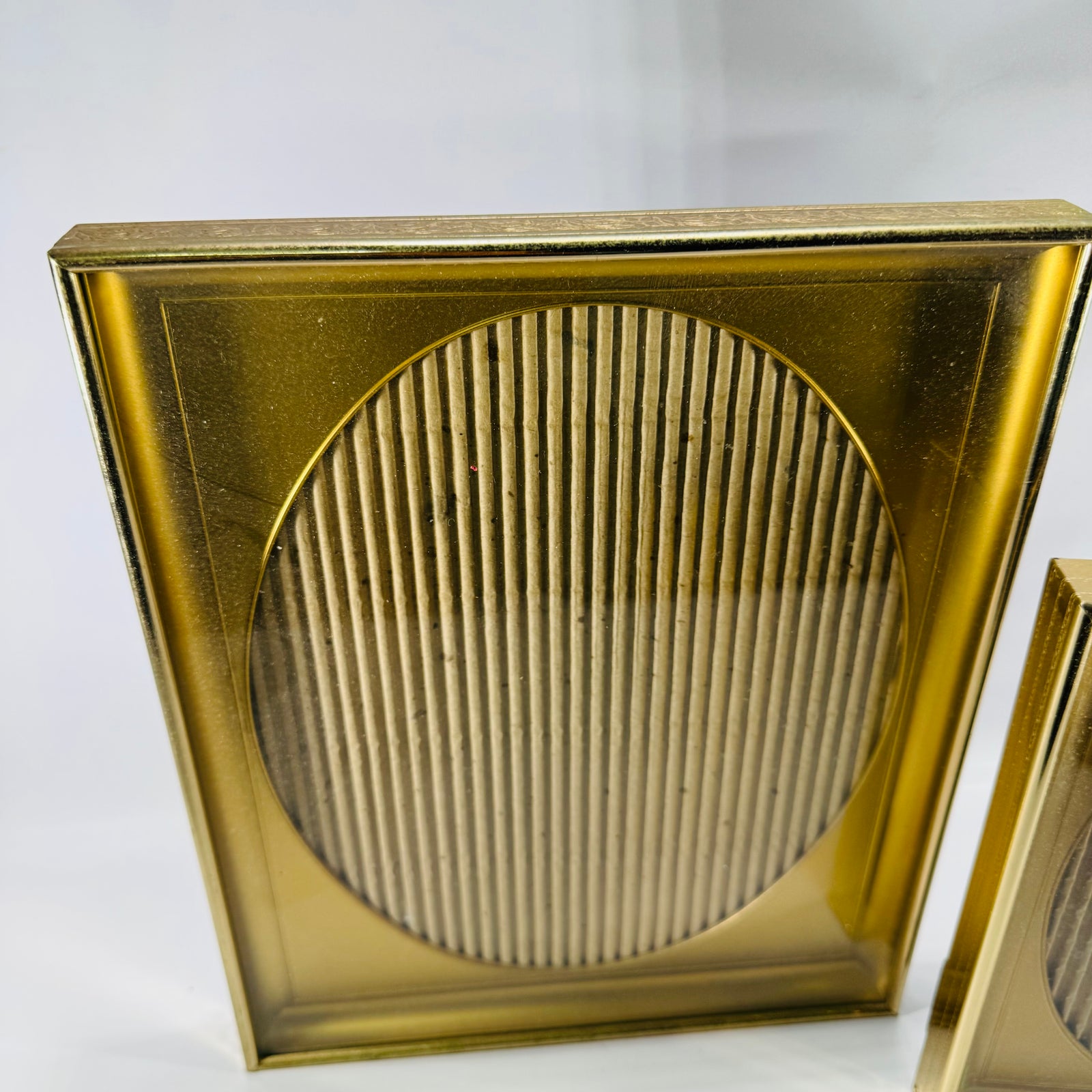 bundle of of two vintage brass-tone shadow box picture frames with oval openings and ribbed oval inserts, one larger and one smaller, displayed upright.