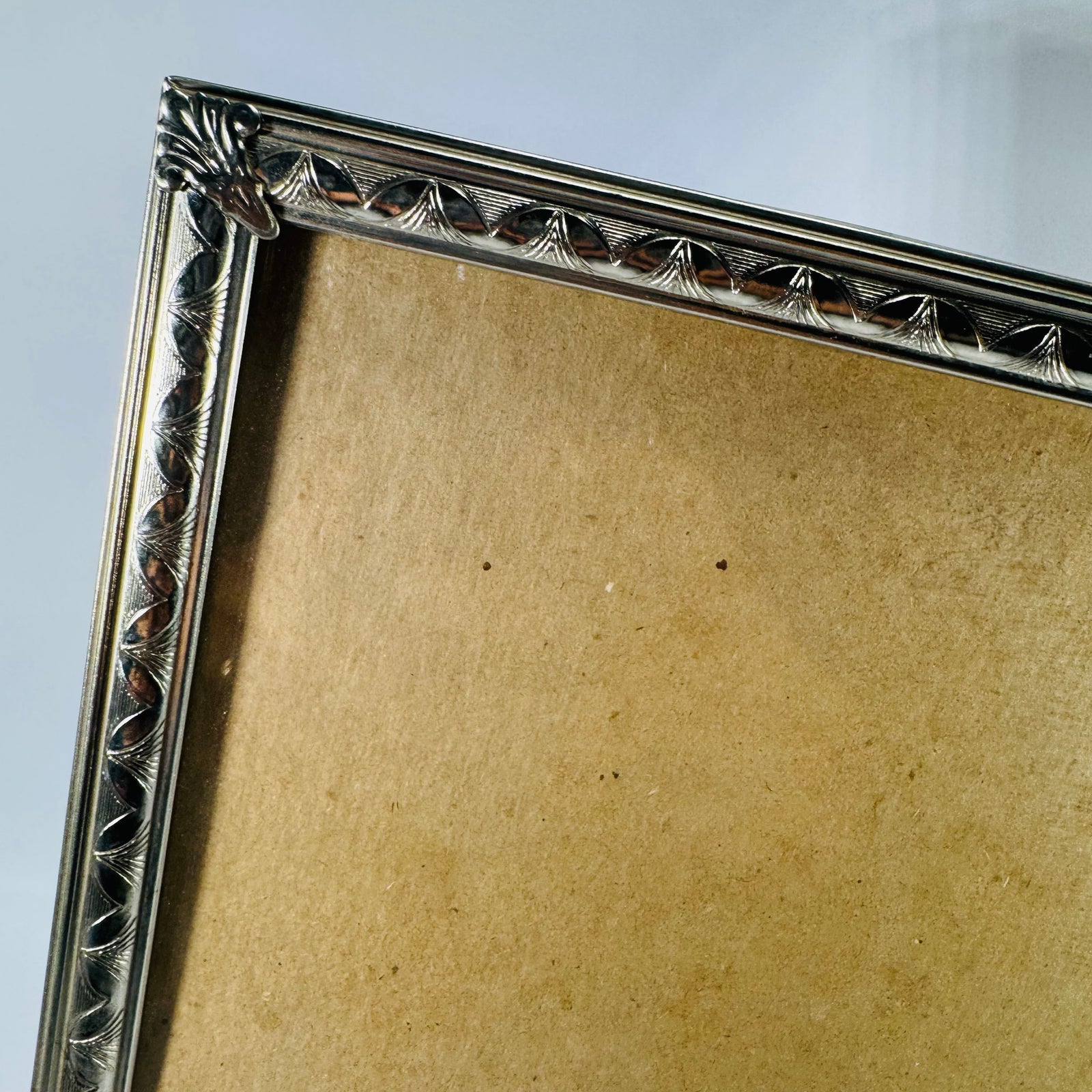 Vintage silver-tone metal 8x10 tabletop photo frame with ornate filigree leaf-and-scroll border, empty insert area shown, standing upright on a white background.
