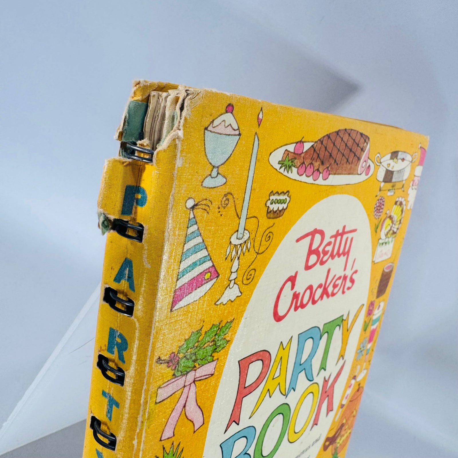 1960 Betty Crocker’s Party Book—bright yellow illustrated ring-bound vintage cookbook with colorful “PARTY BOOK” lettering and festive icons.