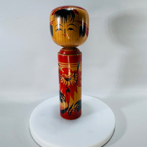 Traditional Japanese kokeshi doll, 7 inches tall, with a red floral painted body and smiling face, photographed standing upright