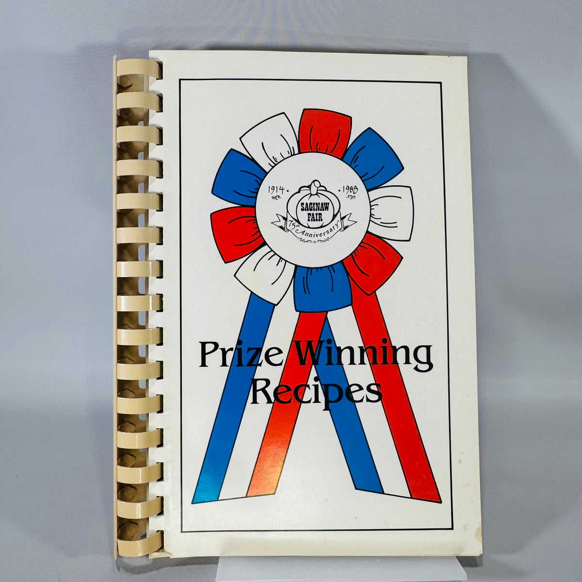 Prize Winning Recipes” (1988 Saginaw Fair) cookbook with red, white, and blue ribbon graphic and 75th anniversary emblem.
