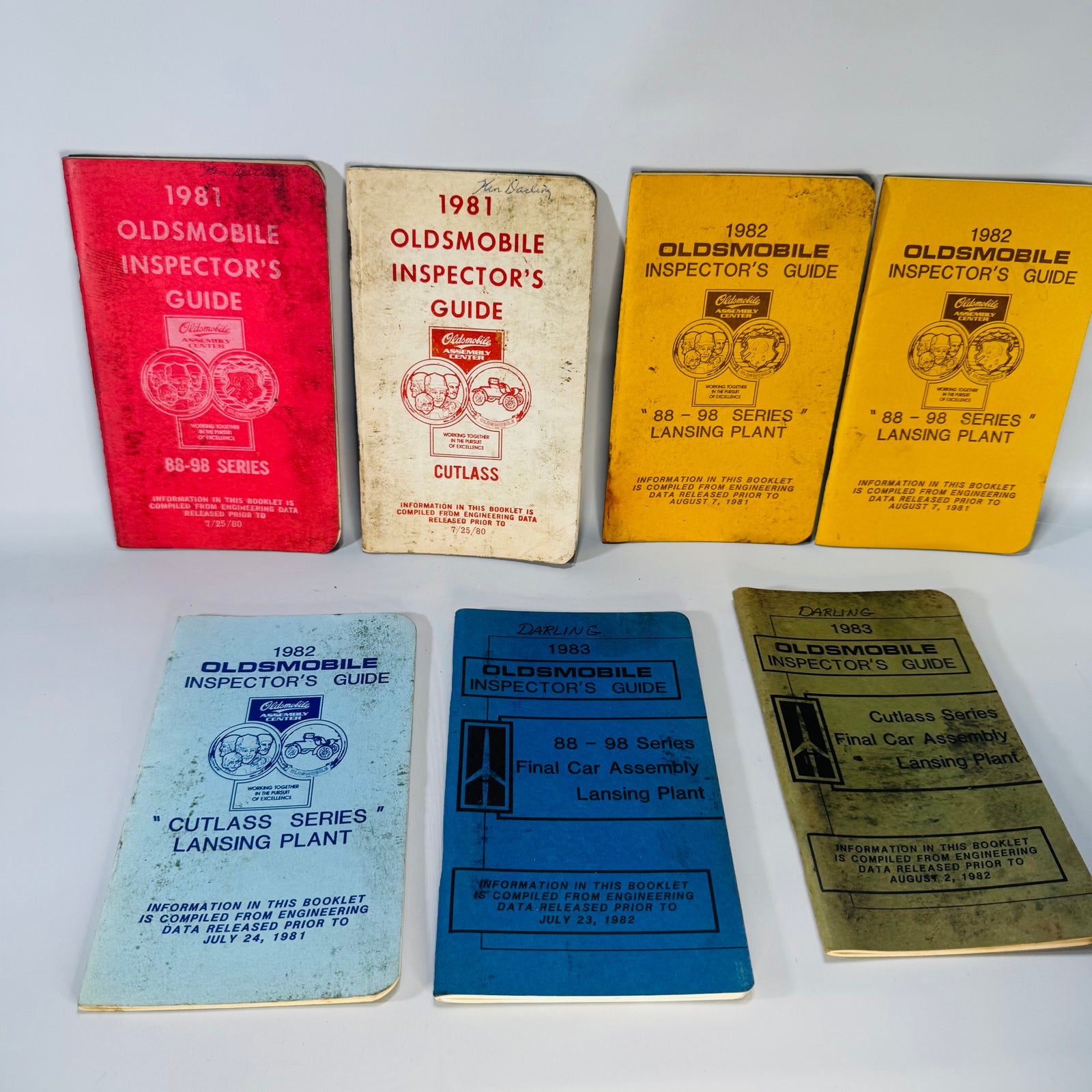 Seven vintage Oldsmobile Inspector’s Guide booklets (1981–1983) in mixed cover colors, stacked and laid out—shop-worn Lansing Plant 88–98 and Cutlass series references.