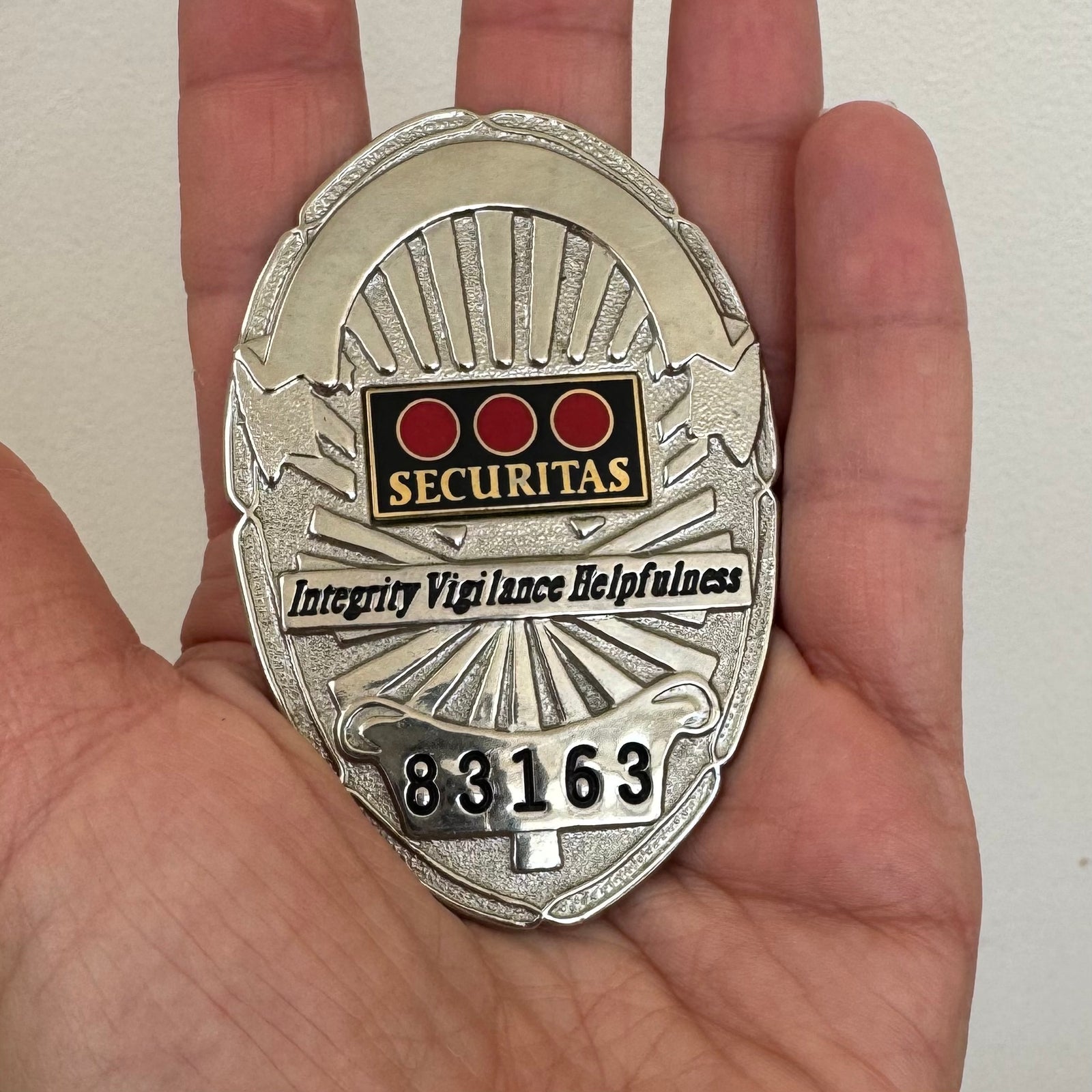  a silver-tone vintage Securitas security badge with three red-dot enamel logo, “SECURITAS” lettering, motto, and badge number 83163.