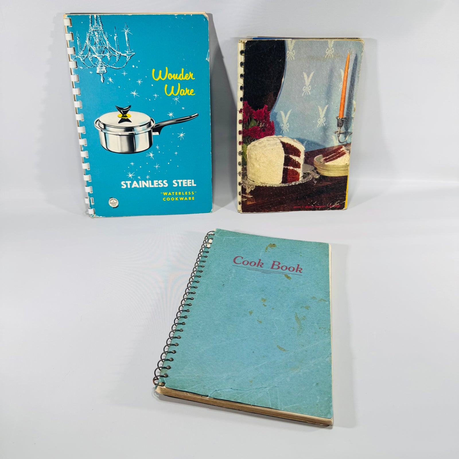 Three vintage cookbooks bundled together: Wonder Ware stainless steel cookware booklet, Jelke’s Good Luck Recipes booklet, and a teal spiral-bound typewritten cookbook on a white background.