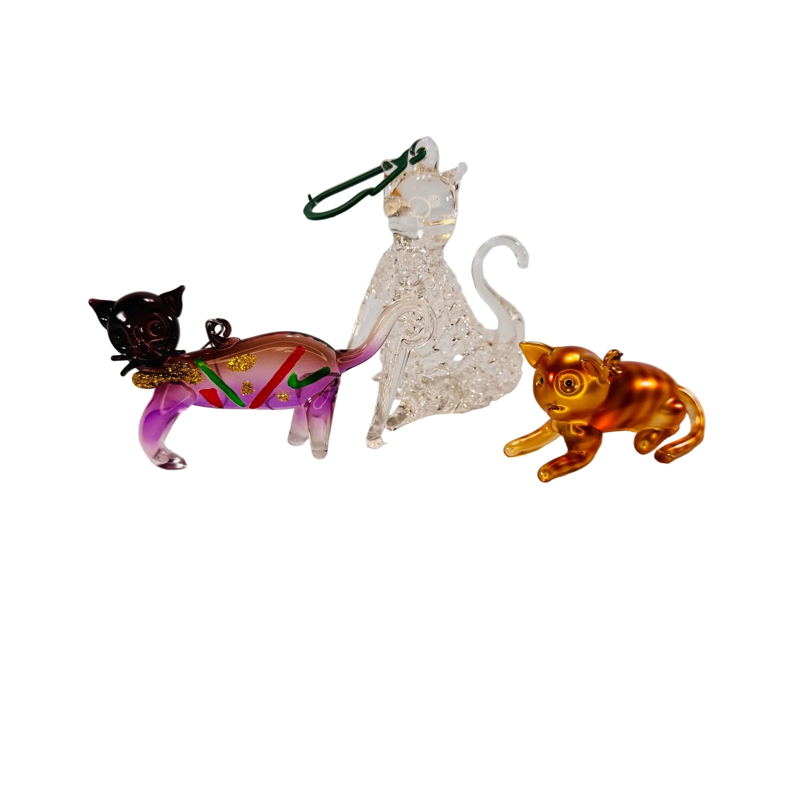Three handblown glass cat ornaments—left: purple cat with red and green accents and gold glitter; center: clear crackle-glass cat sitting upright; right: metallic gold-finish cat in a crouching pose