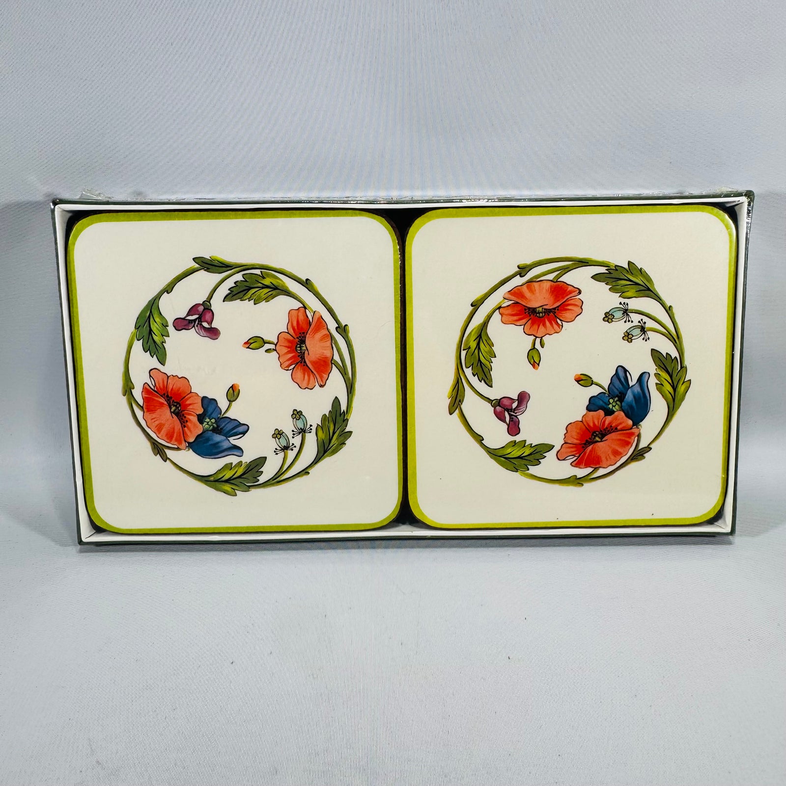 Villeroy & Boch Amapola porcelain coasters in a box, cream background with green border and a floral wreath of red poppies and blue flowers.