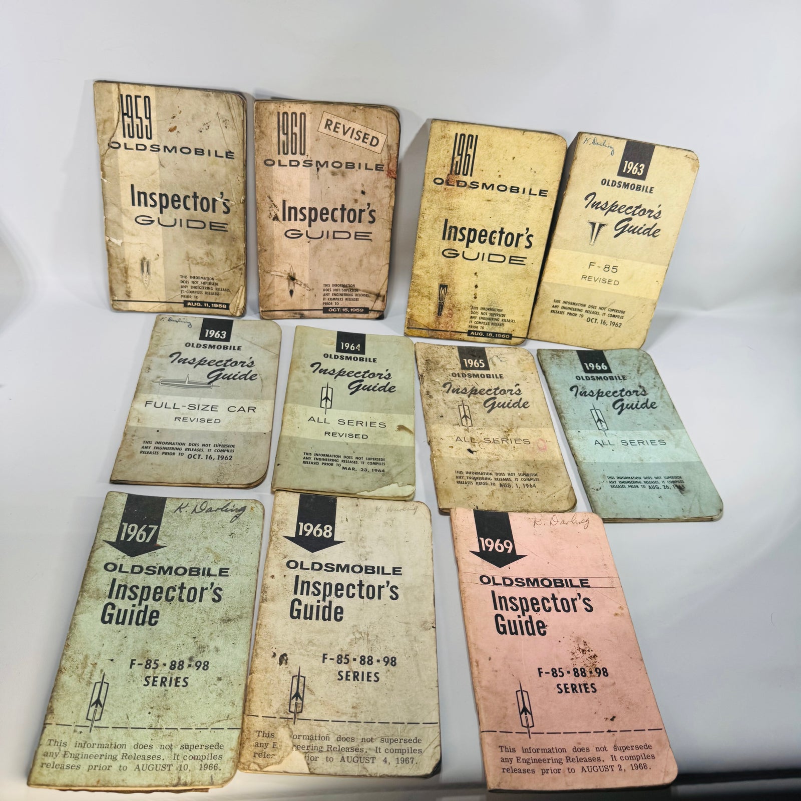 Vintage Oldsmobile Inspector’s Guide lot (1959–1969) with worn pocket manuals—mixed-color covers, shop grime, and quick-reference charts visible inside.