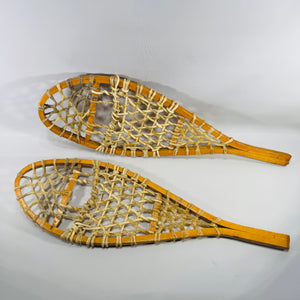 Pair of vintage salesman sample miniature wooden snowshoes with cream rawhide lacing on a white background, 16-inch cabin lodge wall decor.