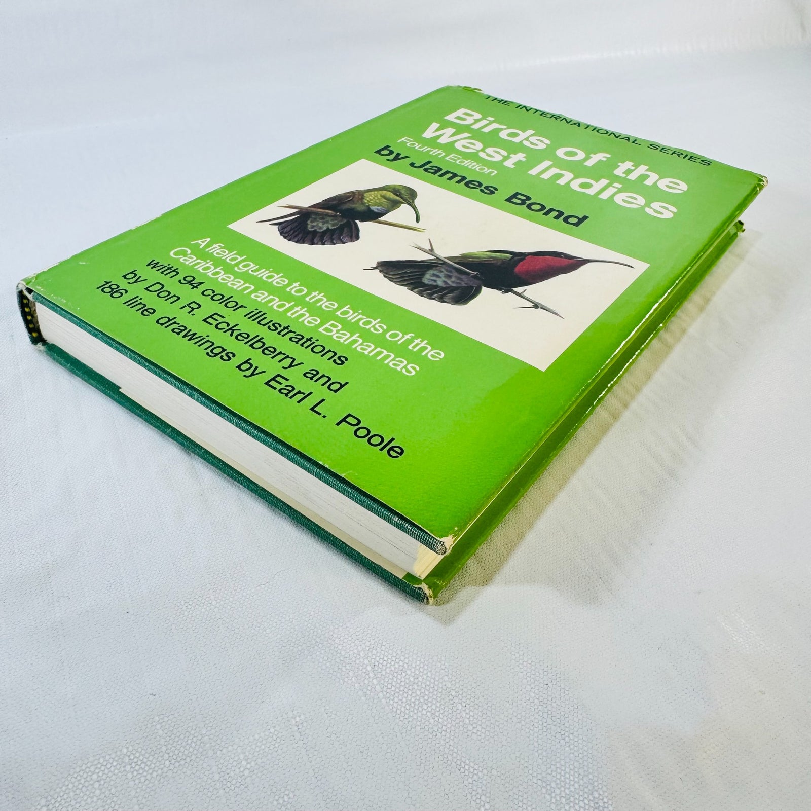 Angled view of Birds of the West Indies by James Bond showing the green illustrated dust jacket, page edges, cloth boards, and corner wear.