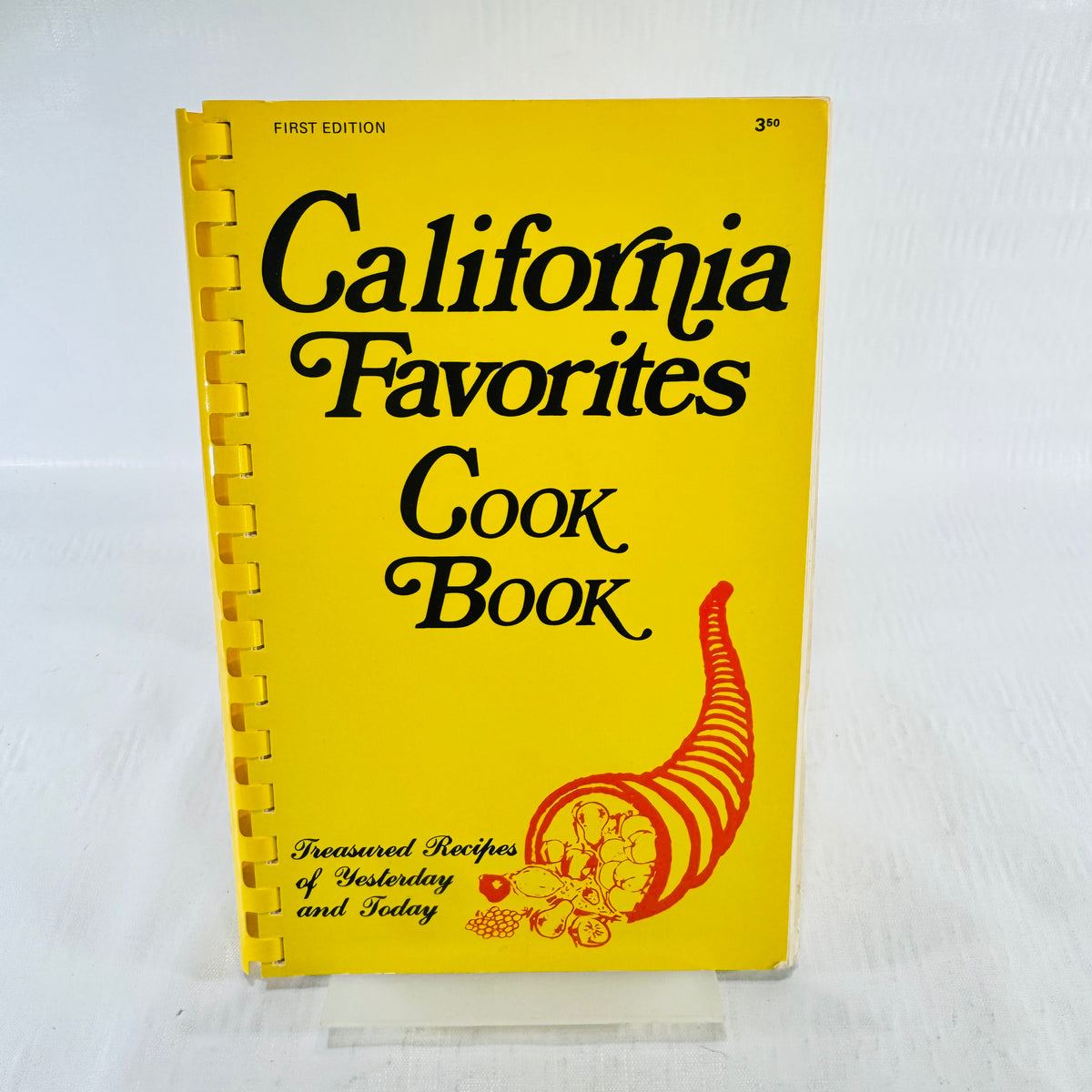 Yellow comb bound front cover of California Favorites Cook Book marked First Edition