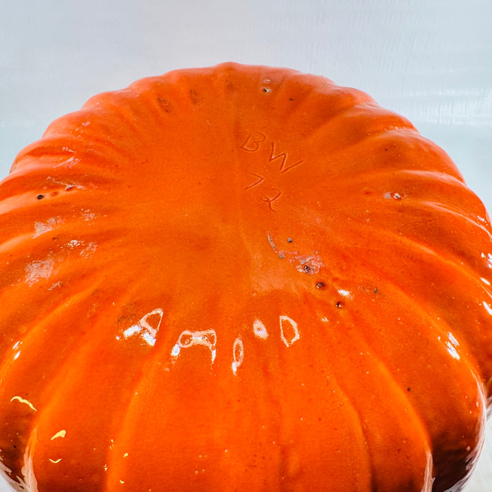 Base of the orange ceramic pumpkin jar showing small glaze specks and pinholes