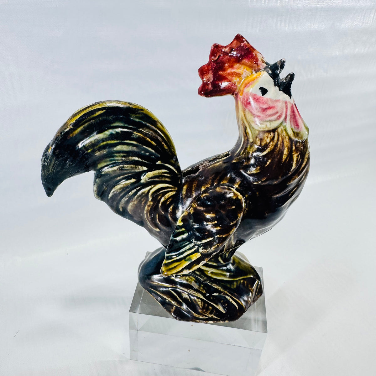 Side view of a ceramic rooster coin bank in glossy brown, green, and yellow drip glaze with a red comb.