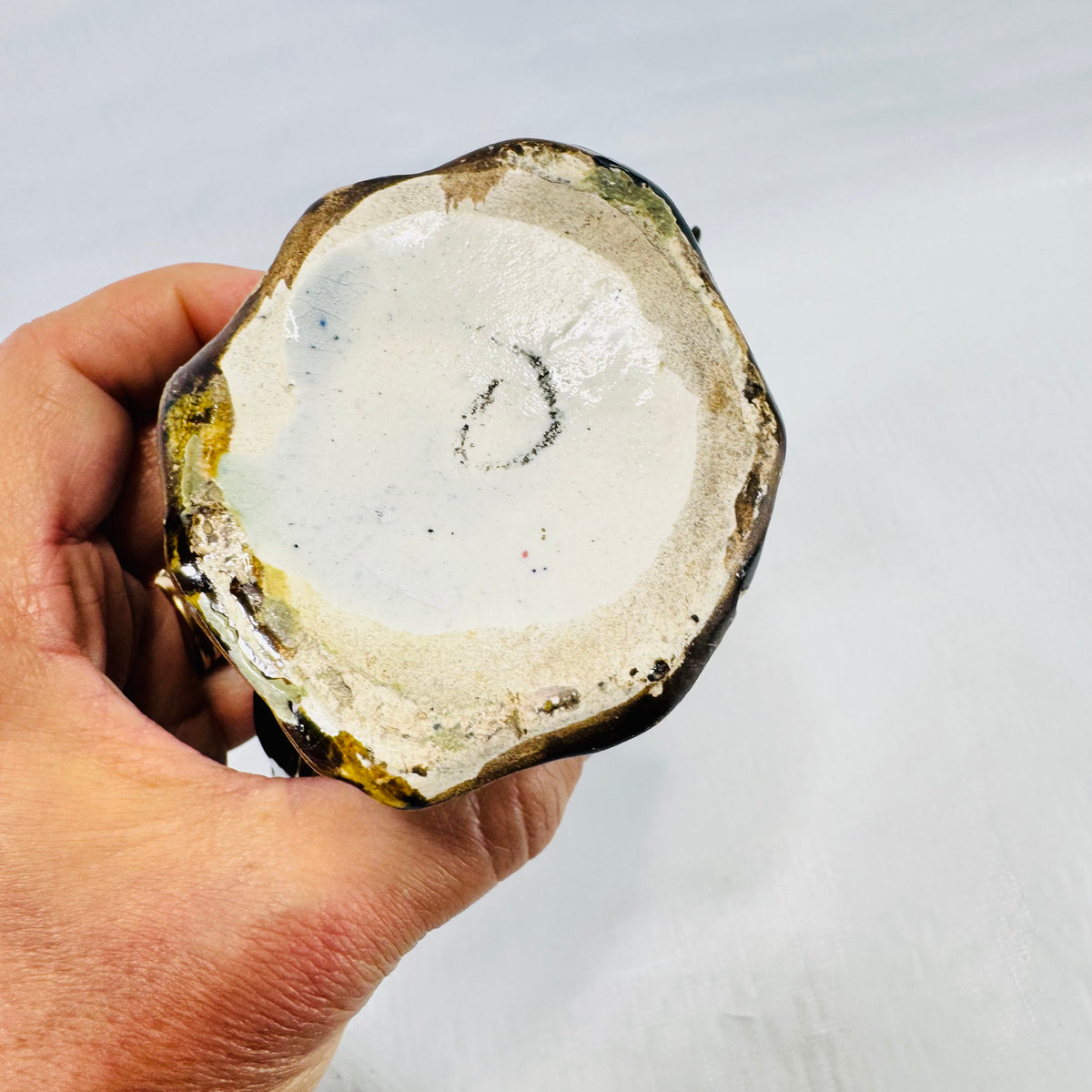 Unglazed white clay underside of the rooster bank with a faint dark handwritten looking loop mark.
