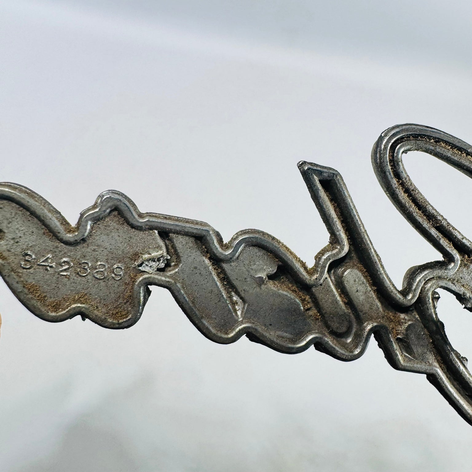 Close view of stamped 342389 part number on Chevrolet grille emblem