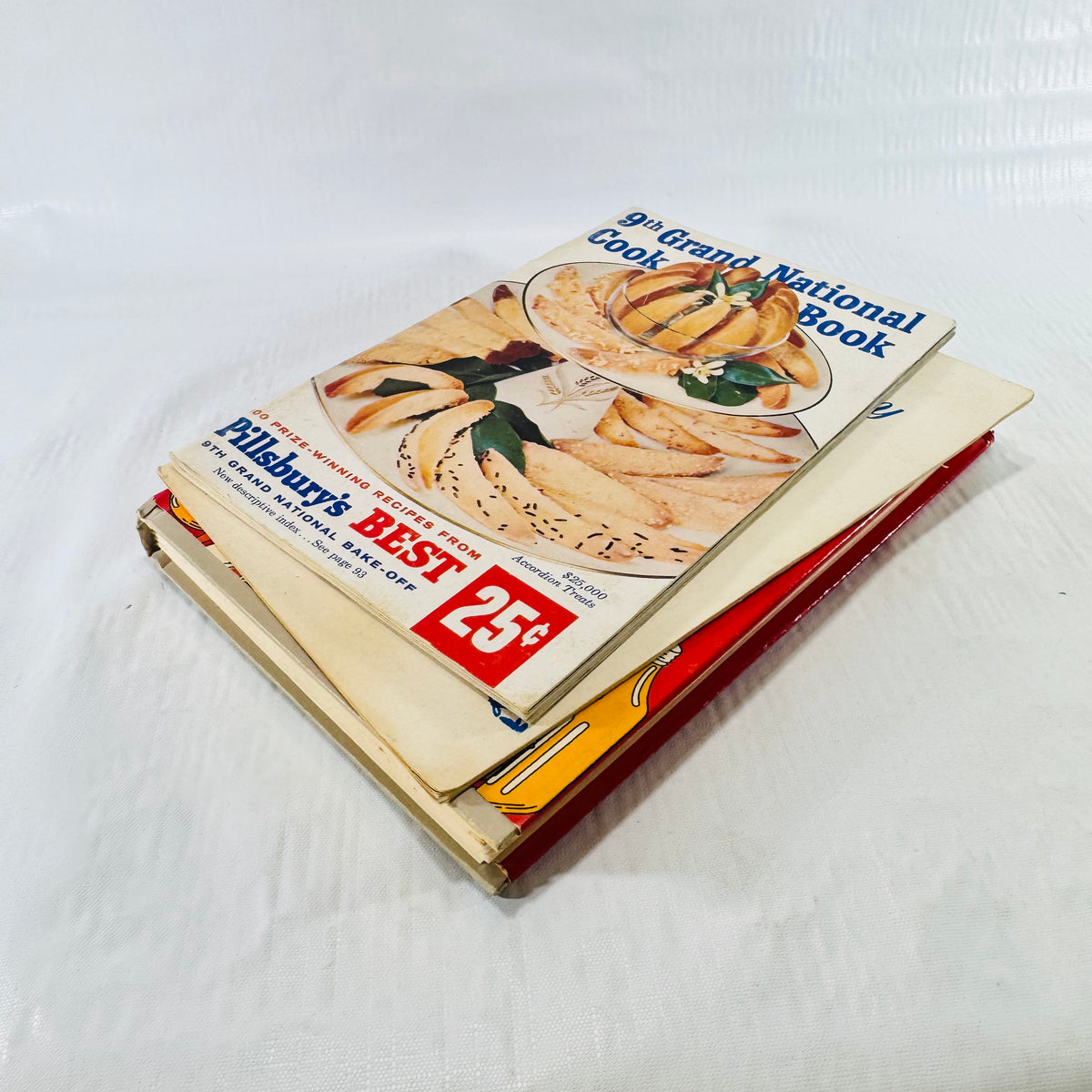 Three cookbooks stacked with the Pillsbury booklet on top