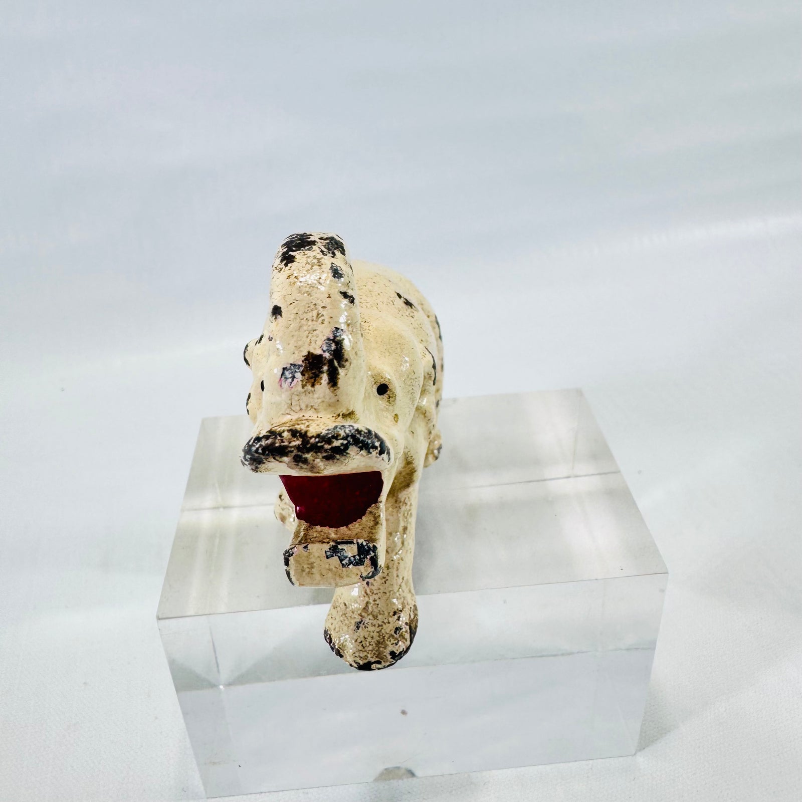 Side view of a cream painted cast metal elephant bottle opener with a raised trunk and black paint chips.