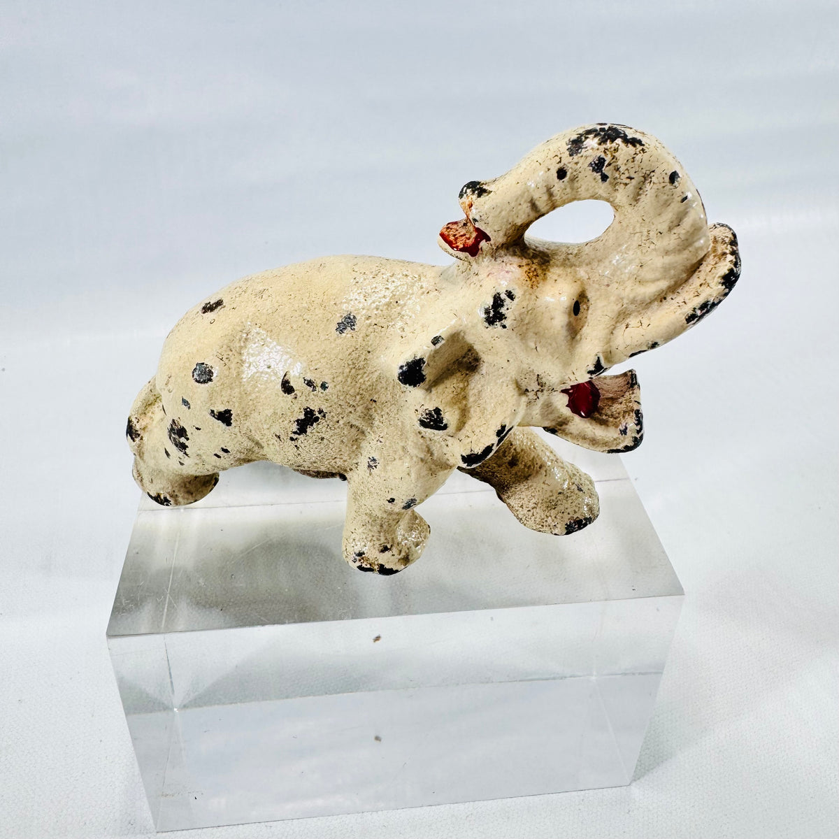 Side view of a cream painted cast metal elephant bottle opener with a raised trunk and black paint chips.