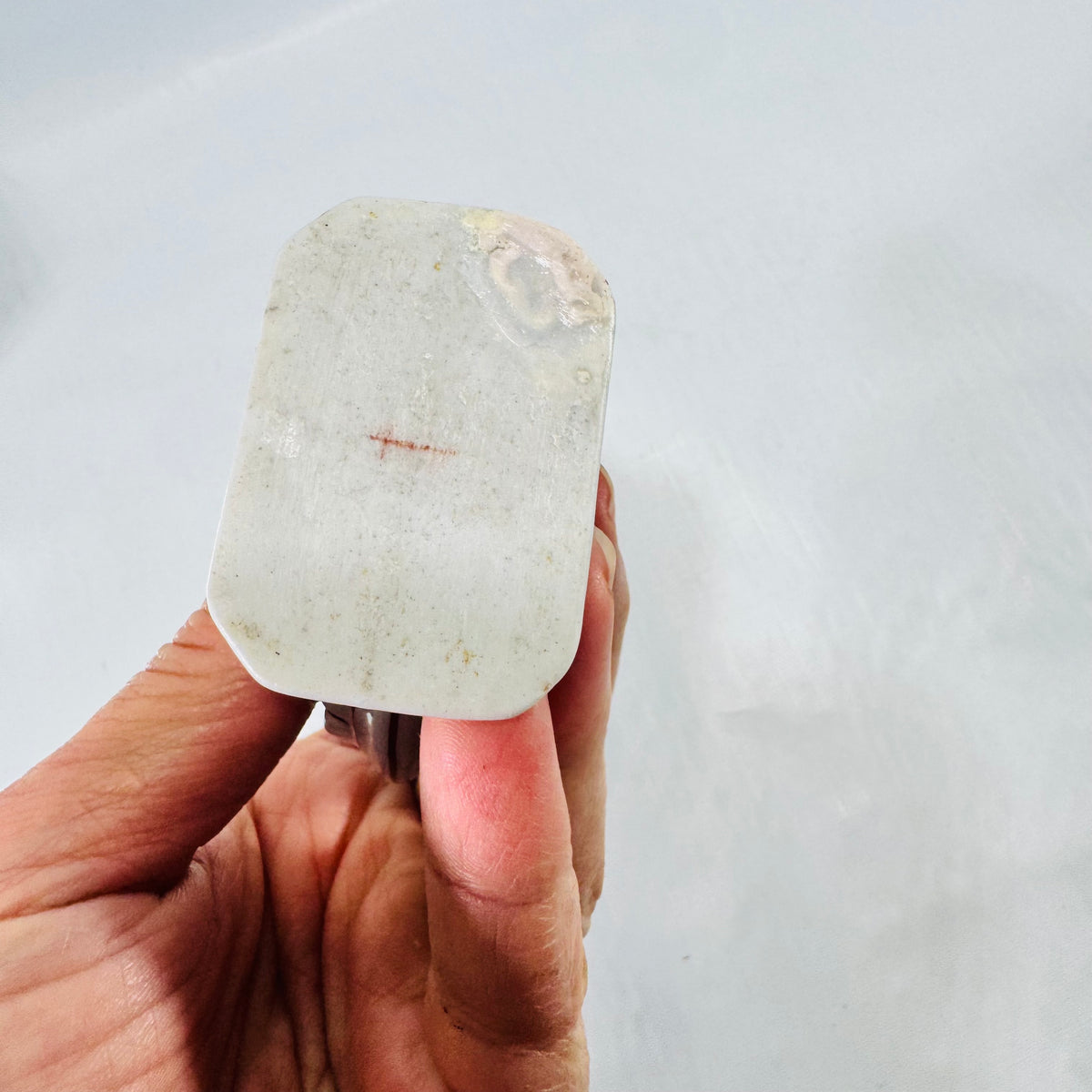 Unglazed foot of the porcelain moon flask bottle with a small red cross shaped mark and a yellowish stain at one corner.