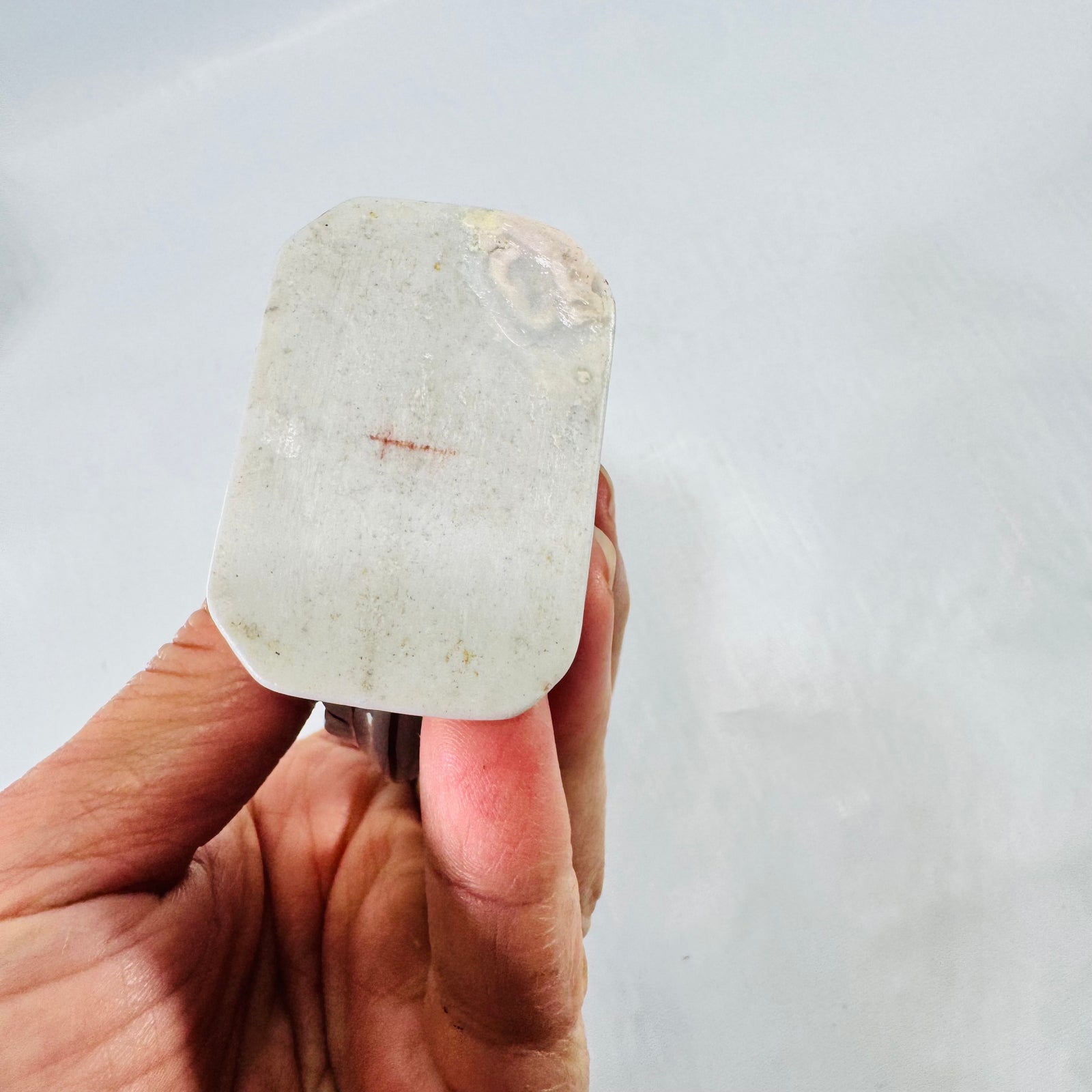 Unglazed foot of the porcelain moon flask bottle with a small red cross shaped mark and a yellowish stain at one corner.
