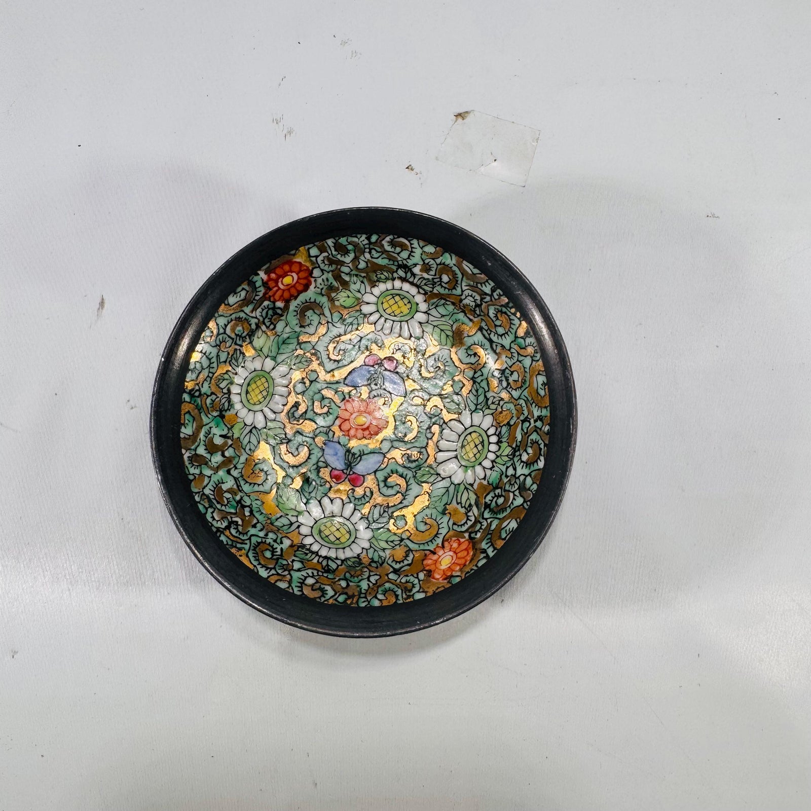 Top-down shot of interior of cloisonné bowl emphasizing scrolling turquoise vines, white daisies, red blooms, and golden accents.