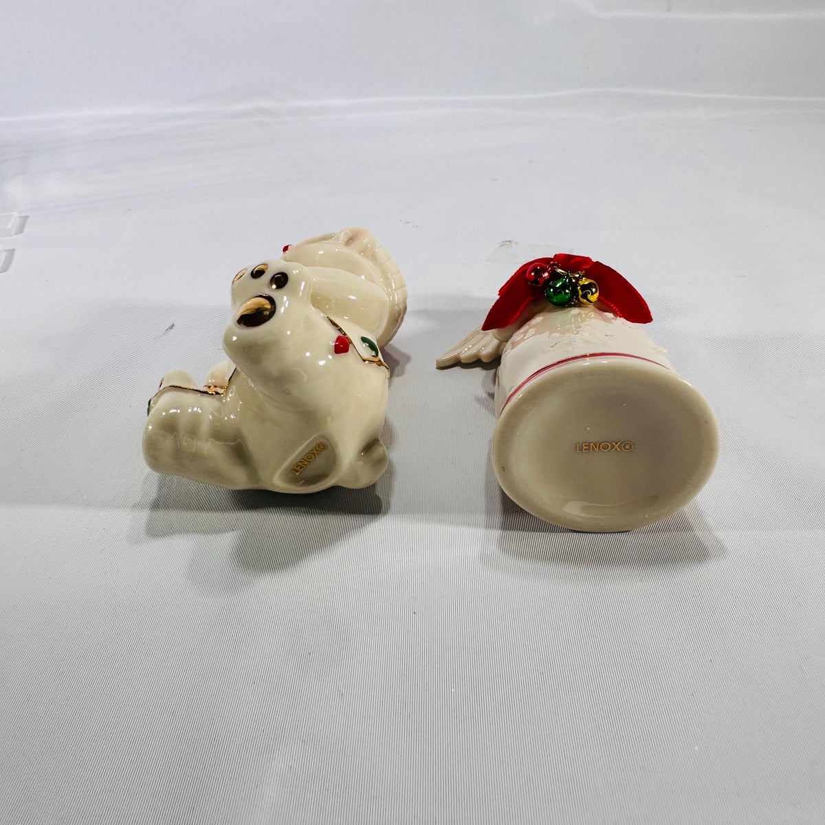 Bottom view of two Lenox® Christmas figurines: a 4″ porcelain angel marked ‘LENOX®’ and a 4″ porcelain teddy bear also marked ‘LENOX®,’ both with hand-painted holiday details and gold accents.