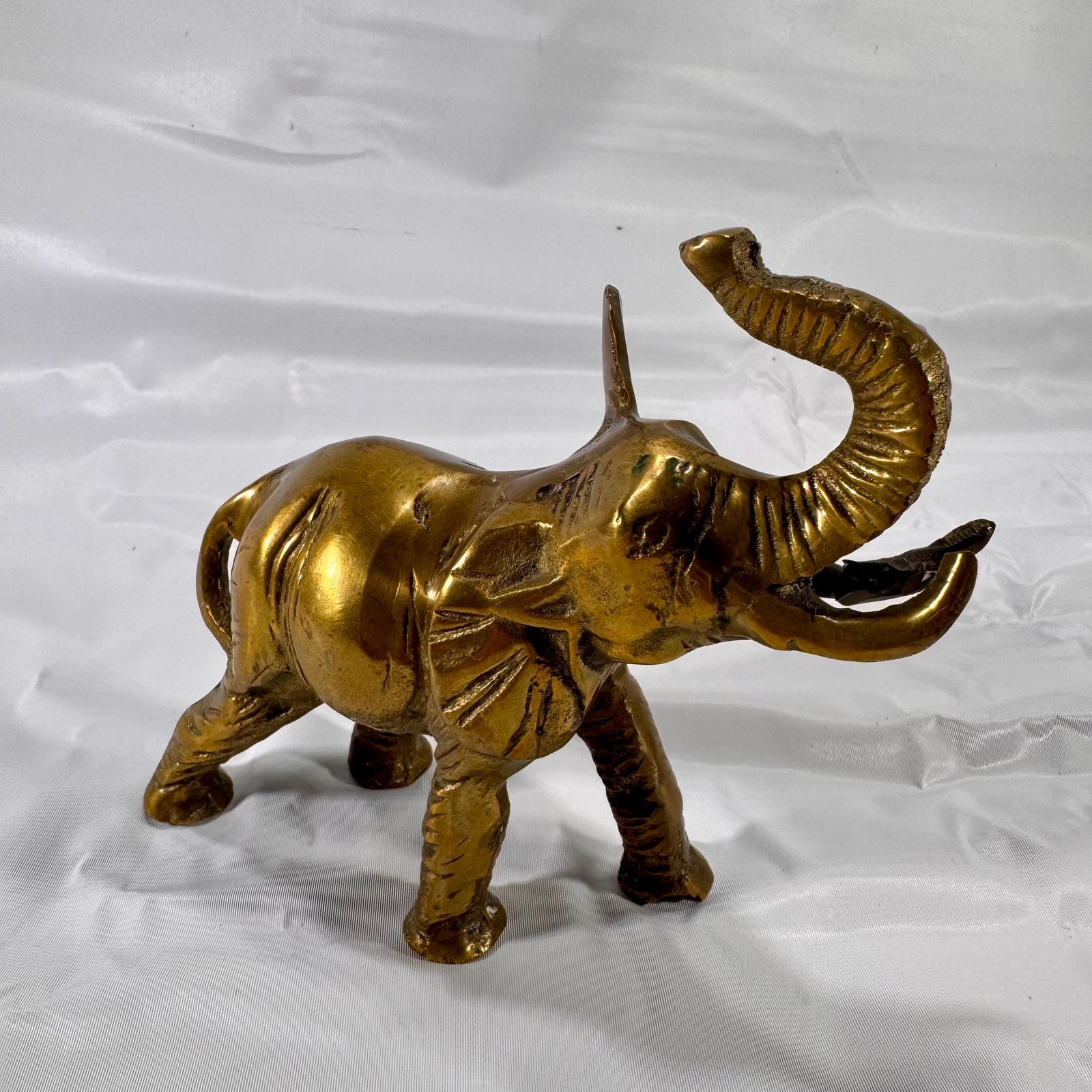 Front left angle view of vintage brass elephant figurine with trunk up, showing overall posture and body detail.
