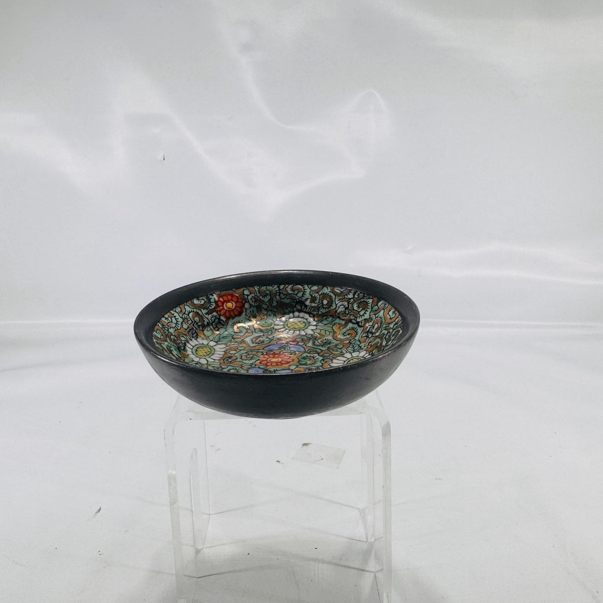 Front view of a small, round cloisonné bowl showing intricate floral enamel design in green, white, red, and gold.